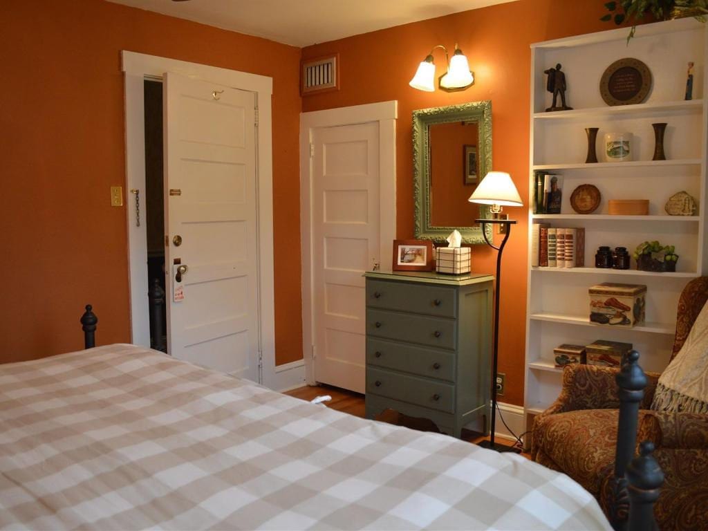 Bedroom with an orange wall and white trim, featuring a bed with a plaid comforter, a green dresser, and a bookshelf.