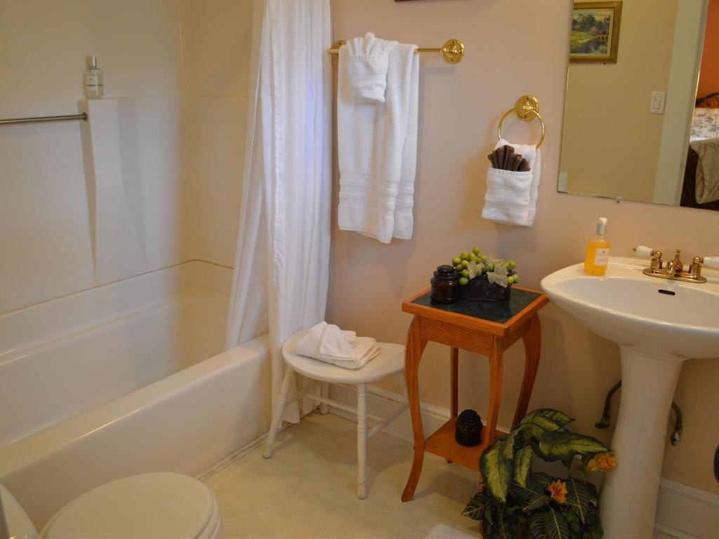 A bathroom with a bathtub, pedestal sink, and decorative table. Towels hang on a bar, and a small stool sits near the tub.