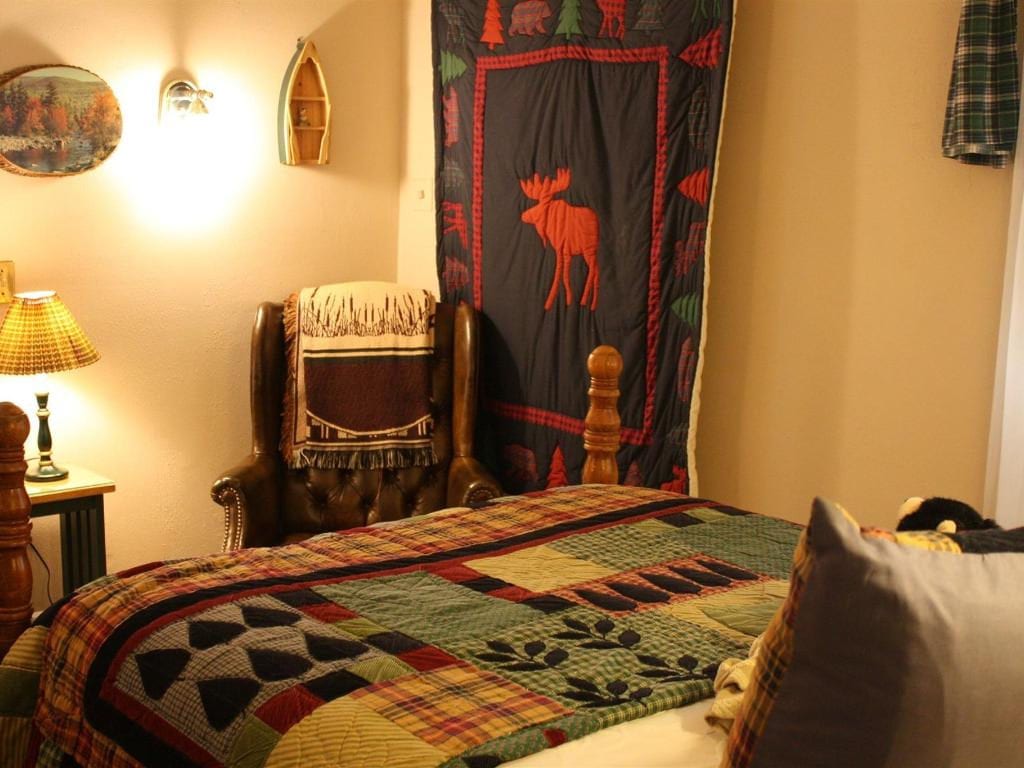 Bedroom with a rustic, cabin-like theme. A bed with a patchwork quilt, a decorative moose tapestry, and wooden furniture are visible.