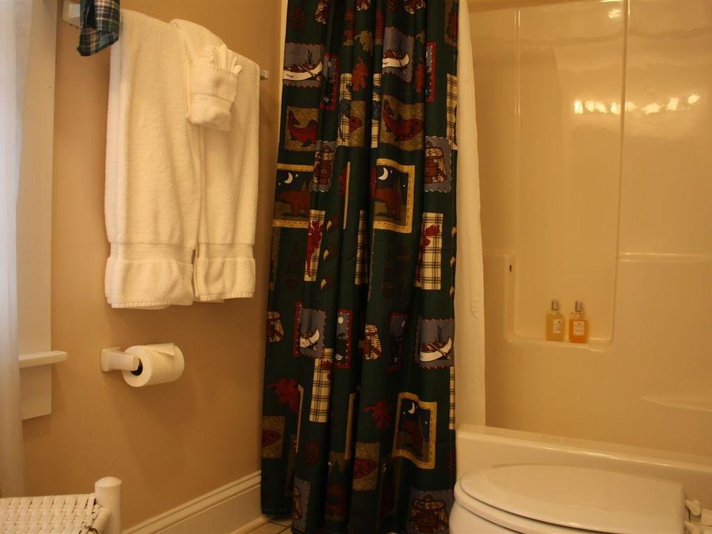 Bathroom with a white tub, toilet, and towels. A patterned shower curtain is drawn. The walls are beige.