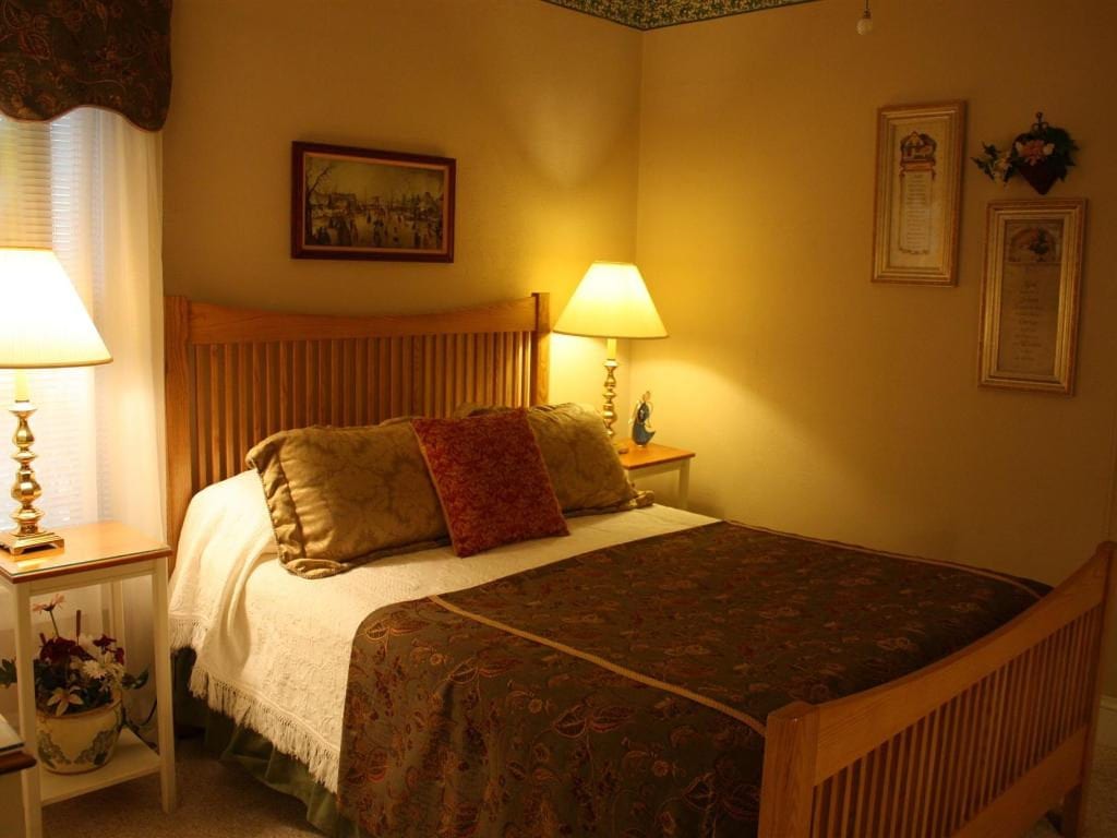 Cozy bedroom with a wooden bed frame, lamps on nightstands, and decorative pillows on the bed. Warm, inviting lighting.