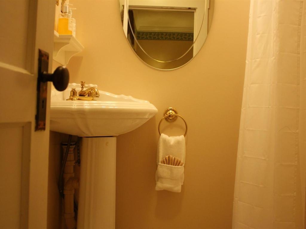 A small bathroom with a pedestal sink, round mirror, and towel ring. A white shower curtain is on the right.