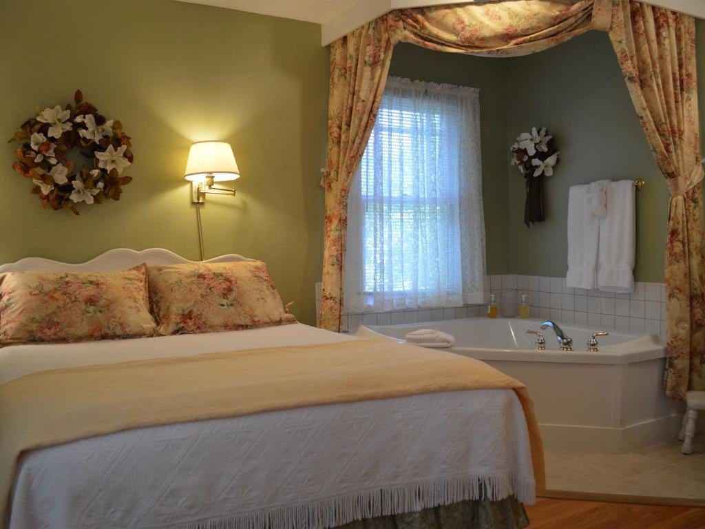 Bedroom with bed, jacuzzi tub, floral wreath, and patterned curtains. Walls are green, with white bedding and accents.