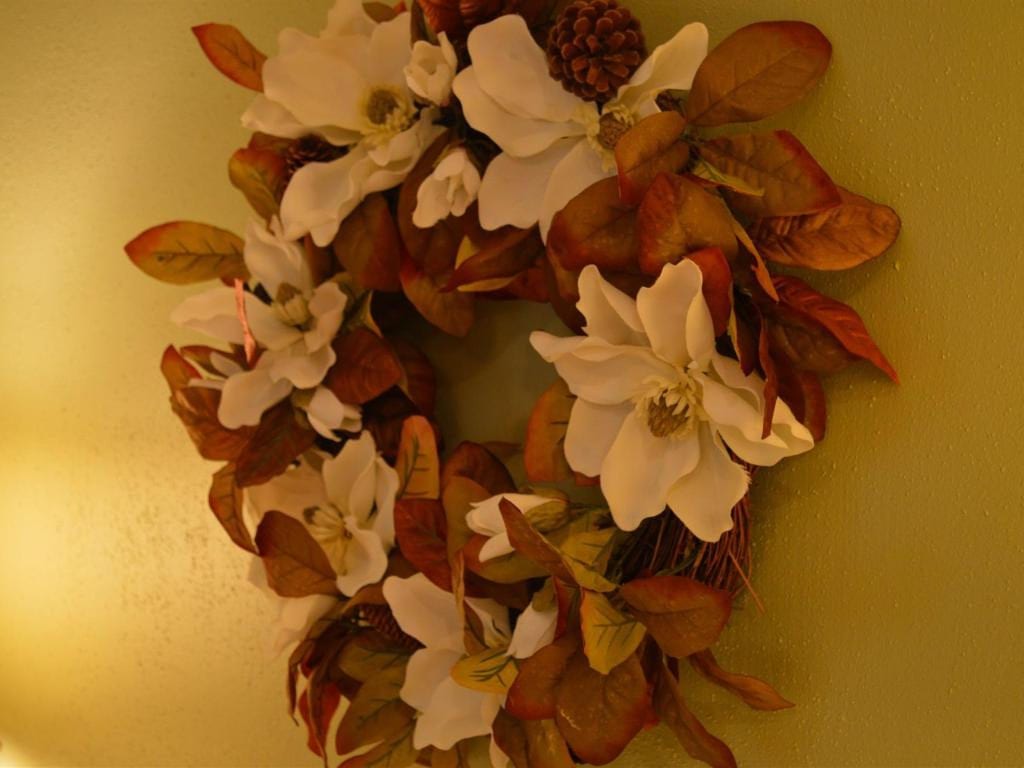 Wreath with white flowers and brown leaves against a light green wall.