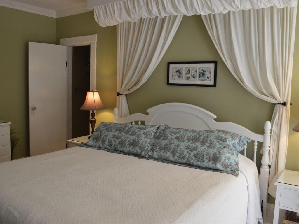Bedroom with white canopy bed, green walls, and floral pillows. A white door is slightly open.