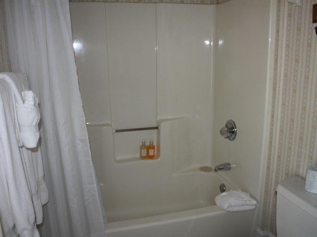 A white bathroom with a tub and shower, a closed shower curtain, and a folded towel on the edge of the tub.