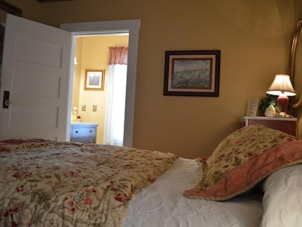 Bedroom with a floral bedspread, partially open door to a bathroom, and a lamp on a bedside table.
