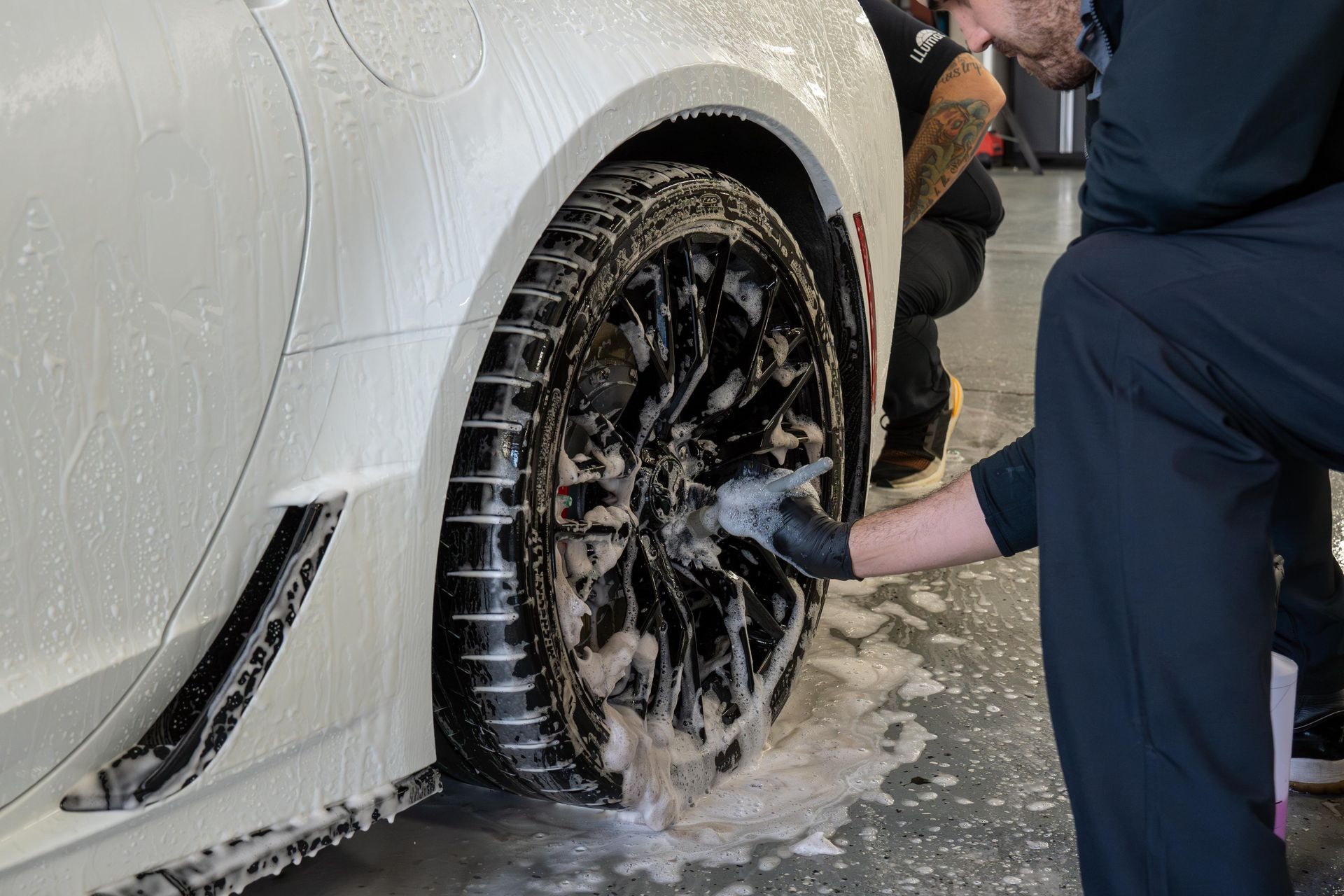 Person washing a black car with soapy sponge outdoors.