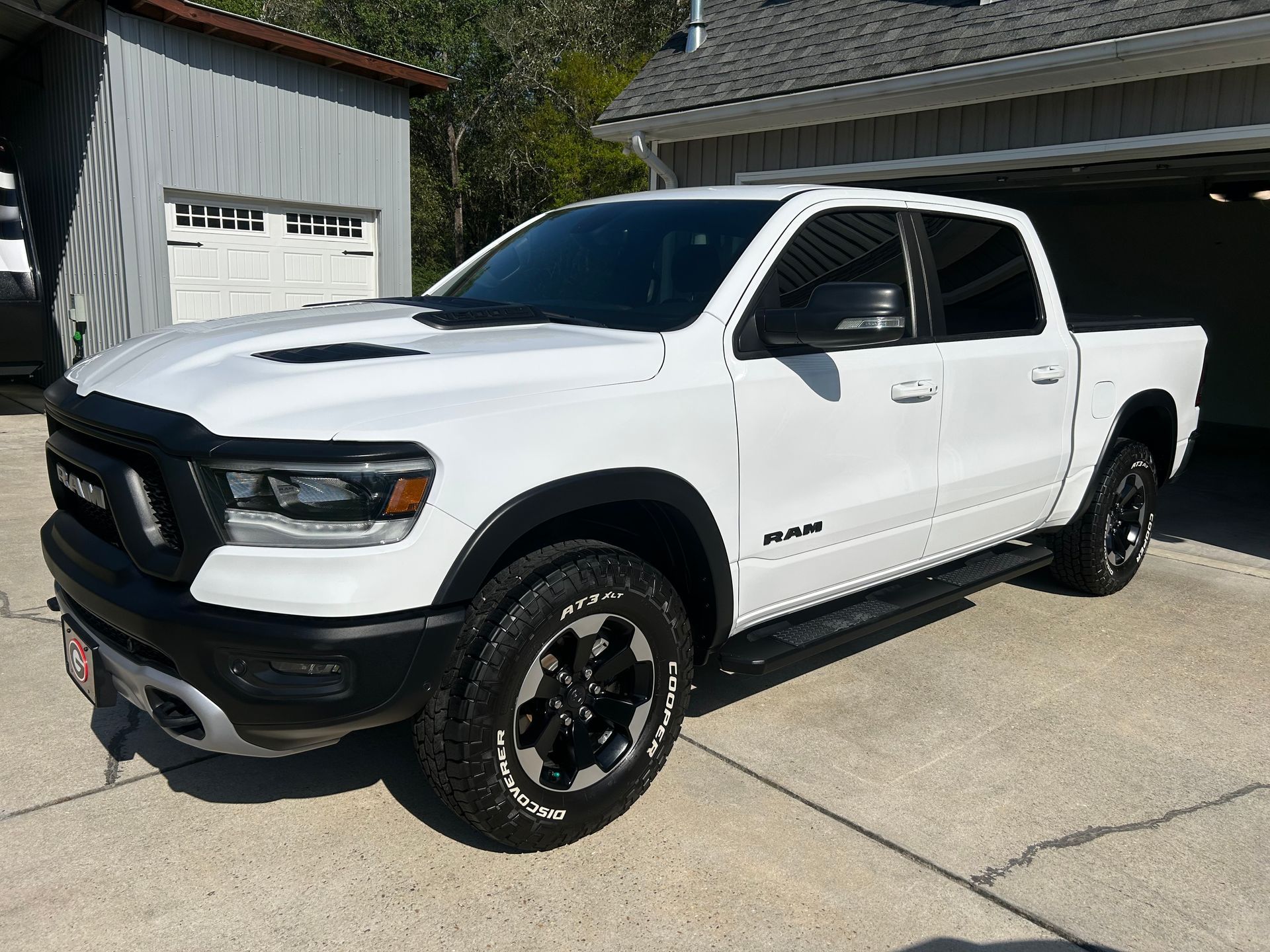 White Ram Rebel pickup truck parked in a driveway. Black accents, black wheels, and a gray building in the background.