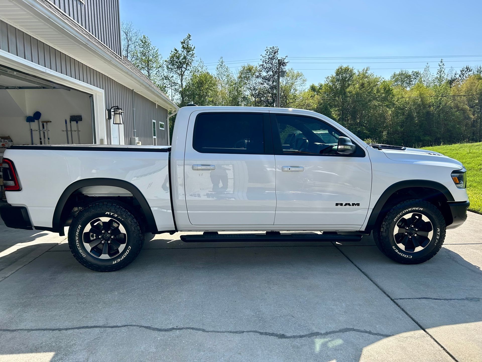 White Ram pickup truck parked on a concrete driveway in front of a house on a sunny day.