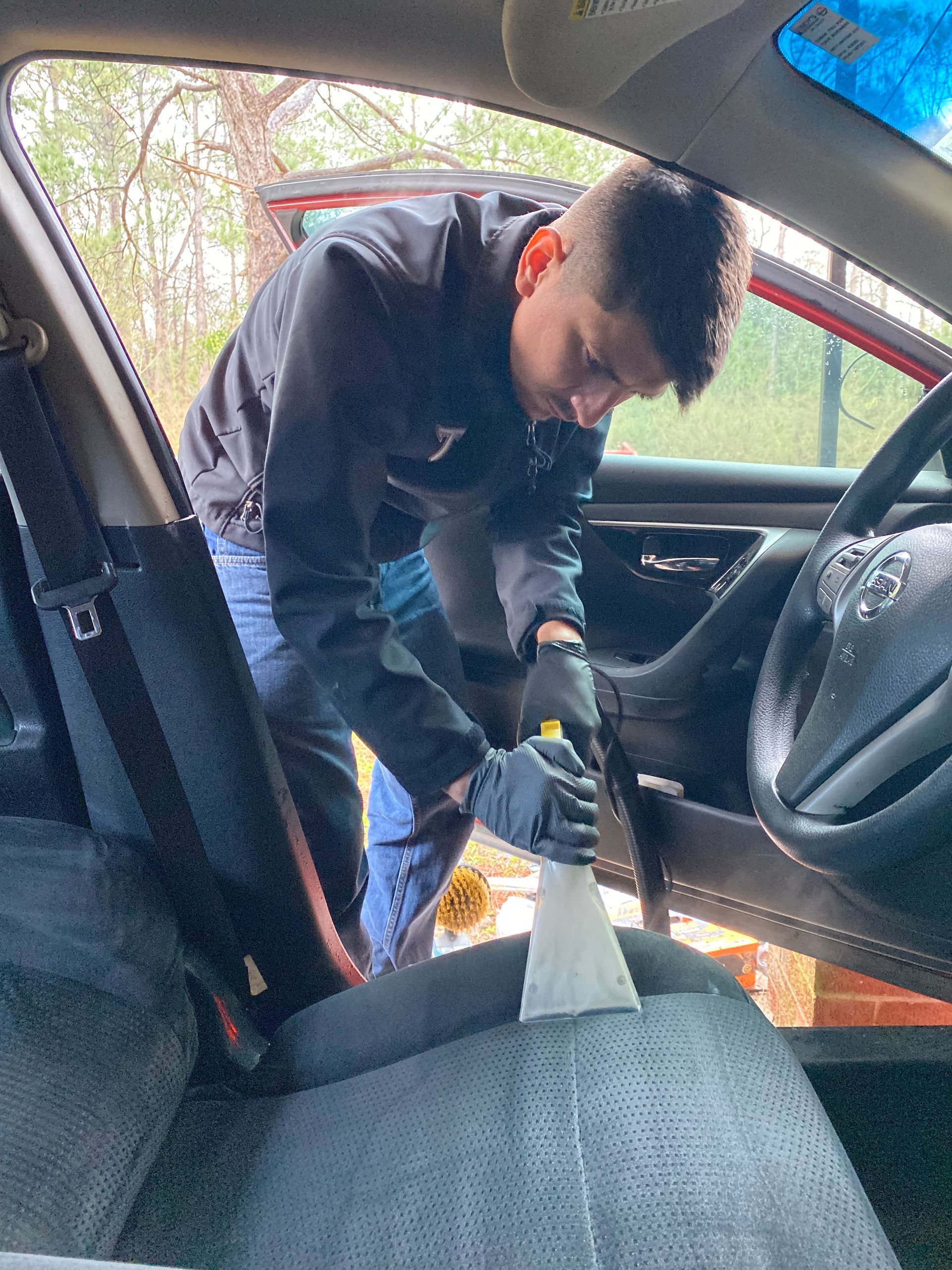 Person vacuuming car seat interior with the open car door.