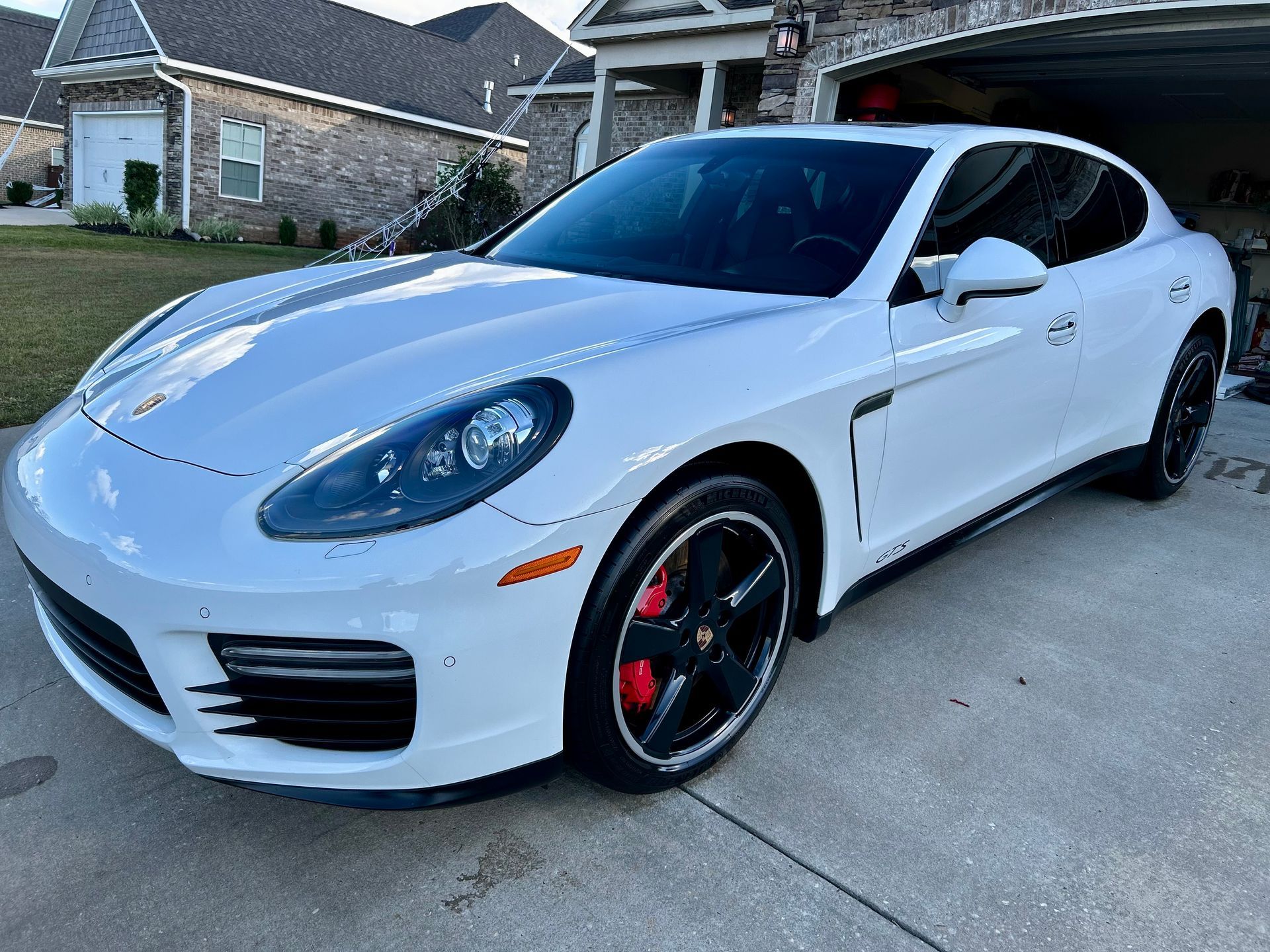 White Porsche Panamera parked in a driveway. Red brake calipers visible behind black wheels.