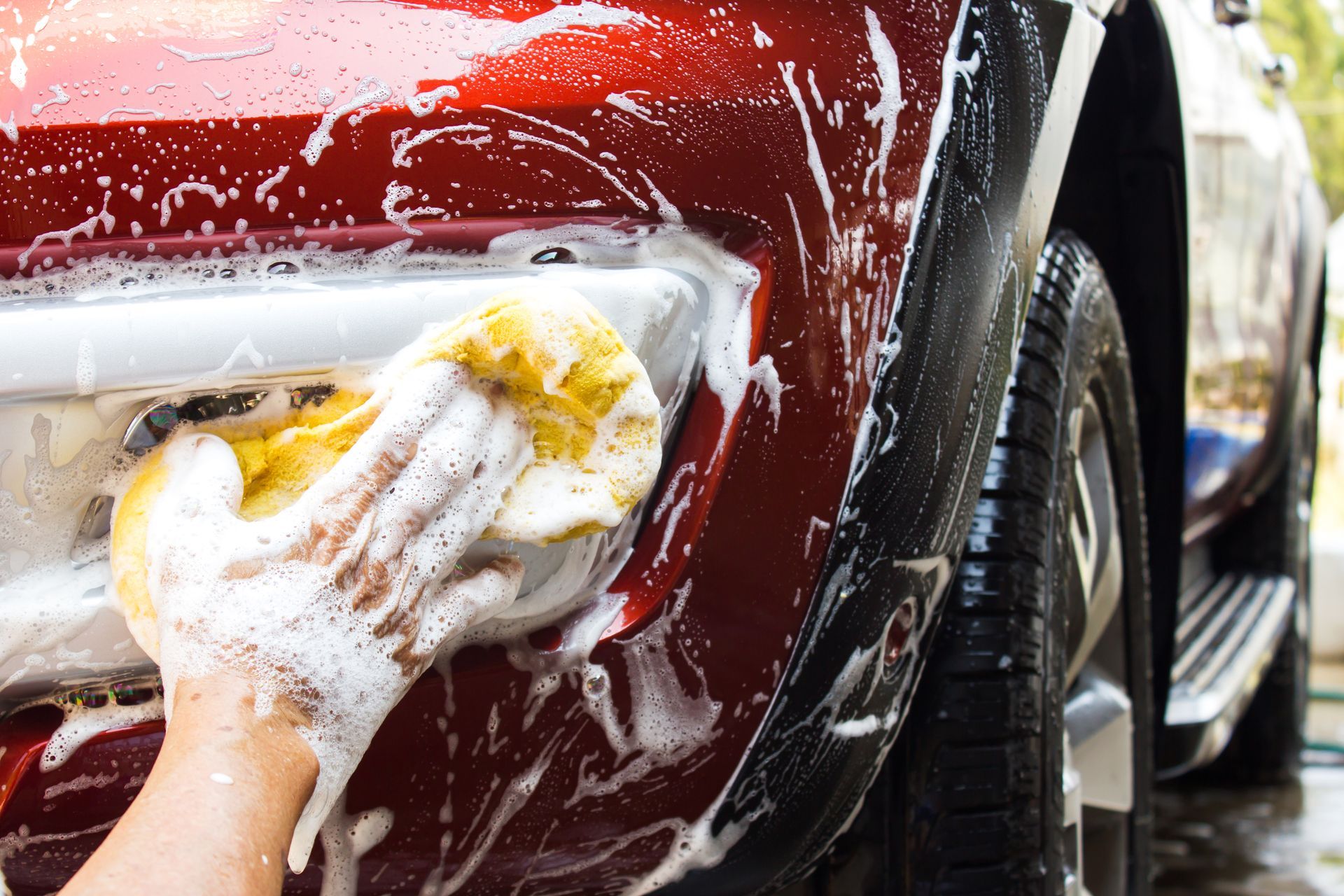 Hand washing a red car with a soapy sponge.