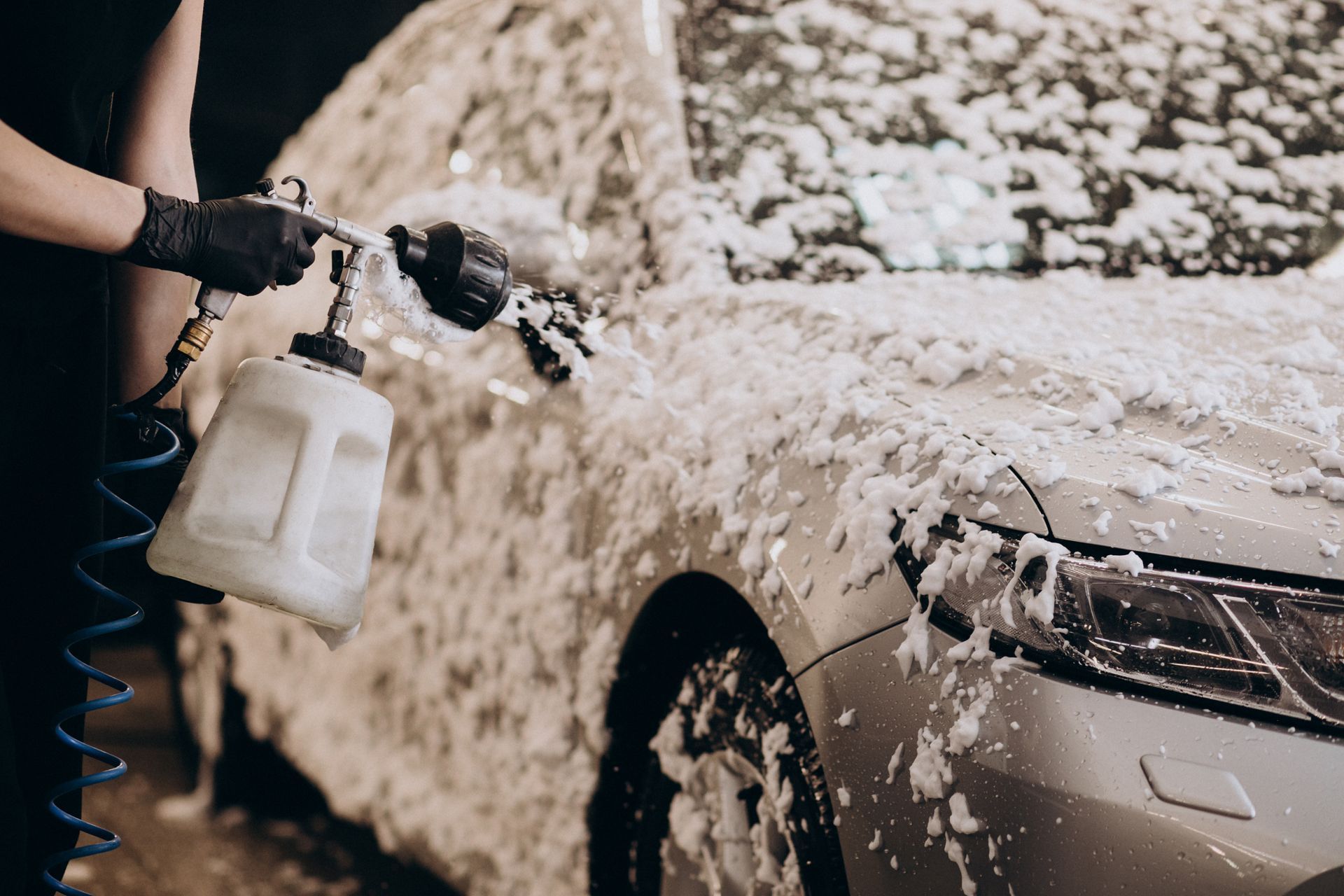 A person wearing black gloves spraying a car wheel with cleaning solution.