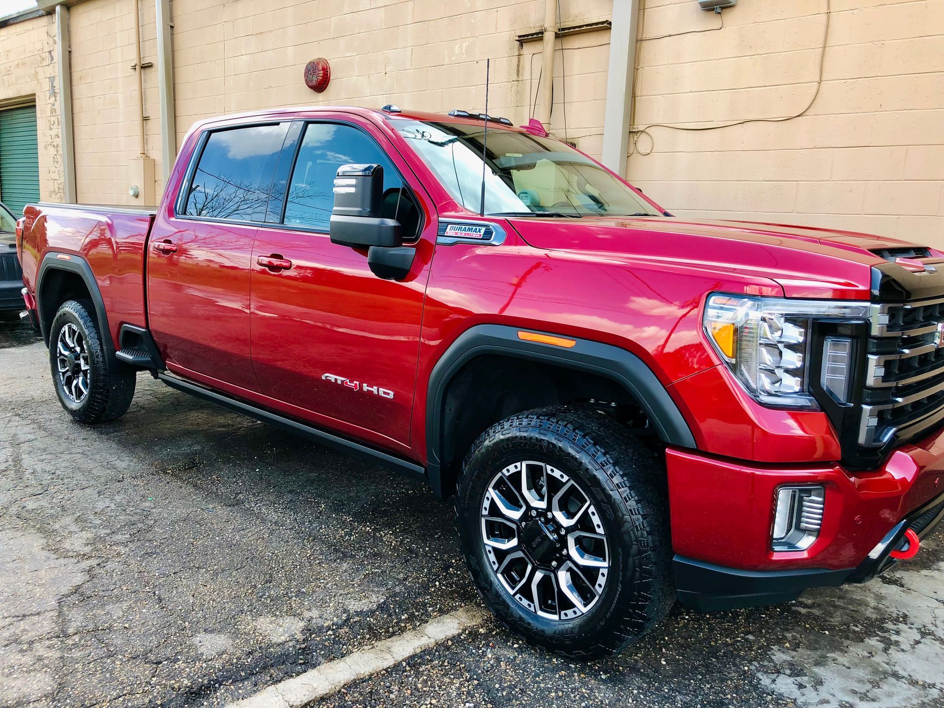 Red GMC truck parked, angled view. Black accents, black and silver wheels, on a gray paved surface.