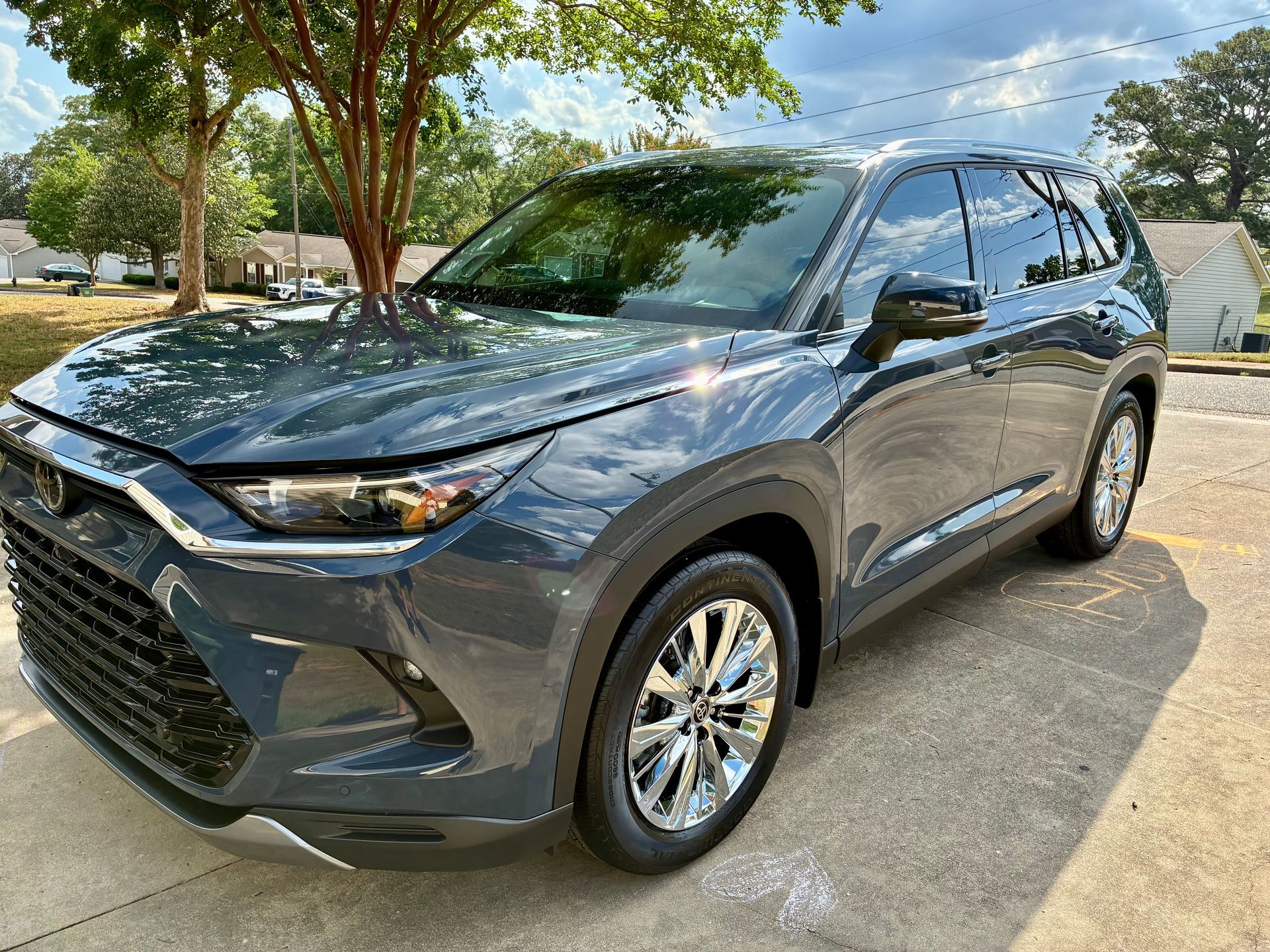Dark gray SUV parked on concrete. Shiny chrome wheels. Outdoors, sunny day.