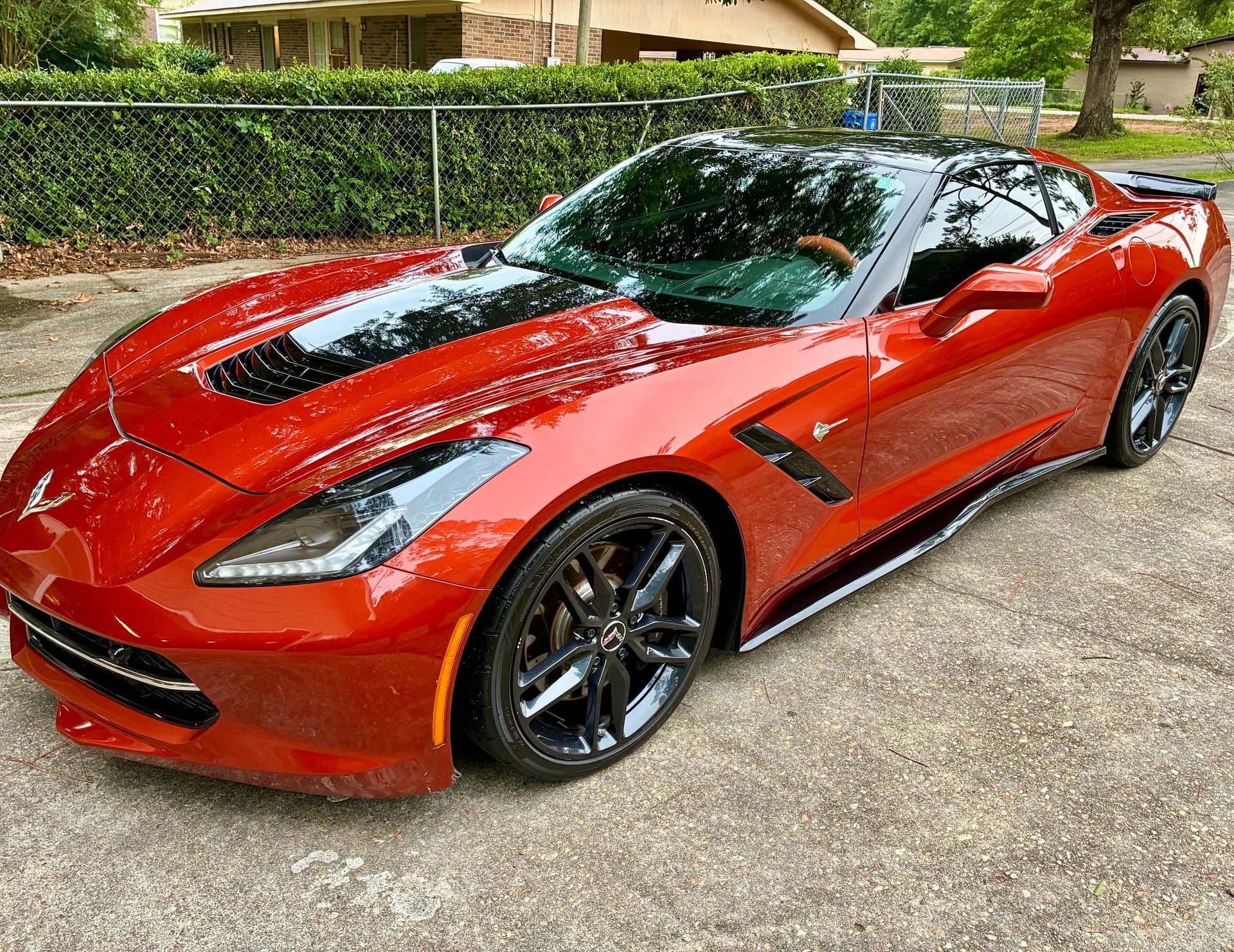 Red sports car parked on a paved driveway with black wheels.