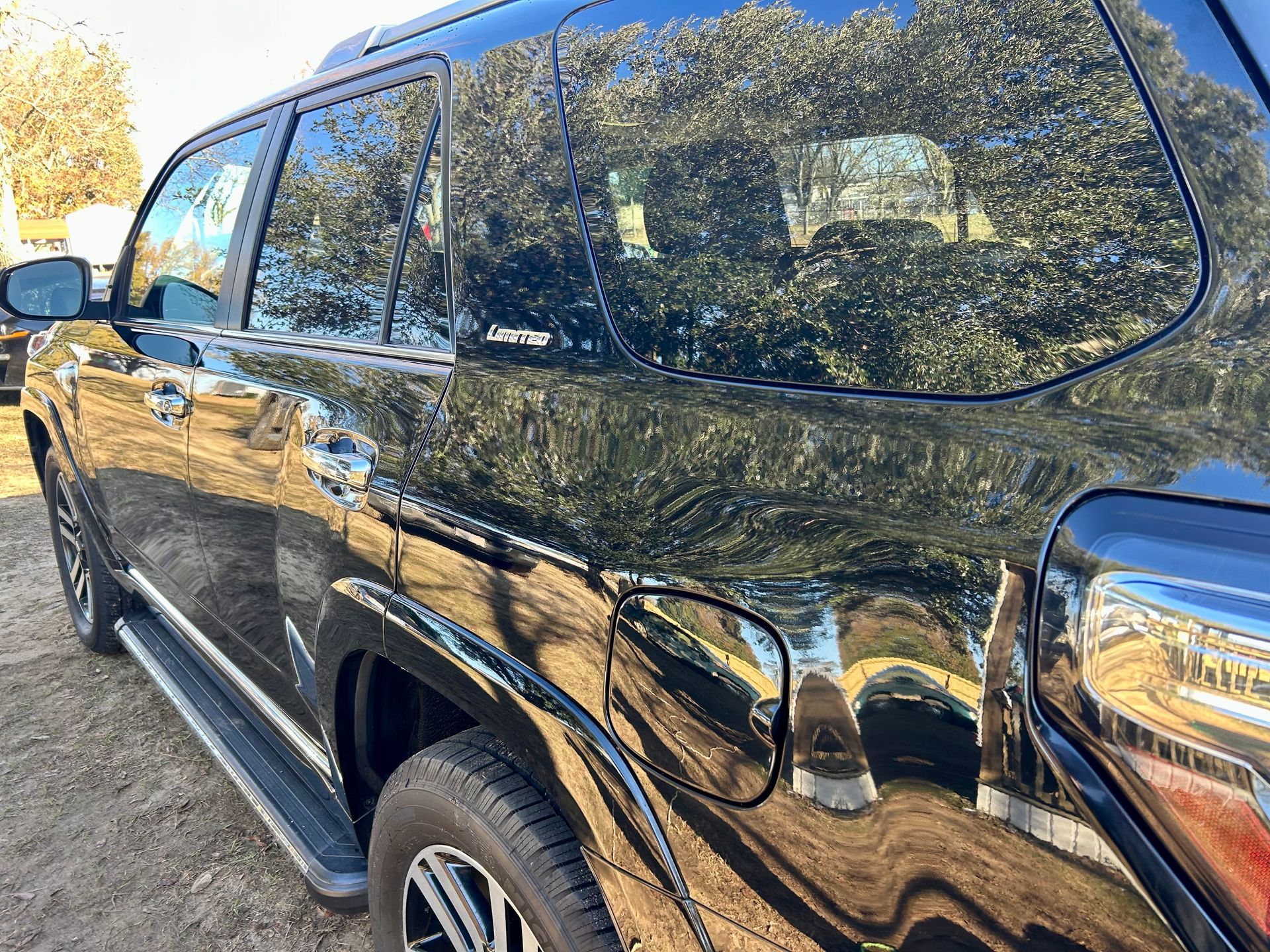 Black SUV, reflecting trees and sky, parked outside on dirt. Fuel door visible.