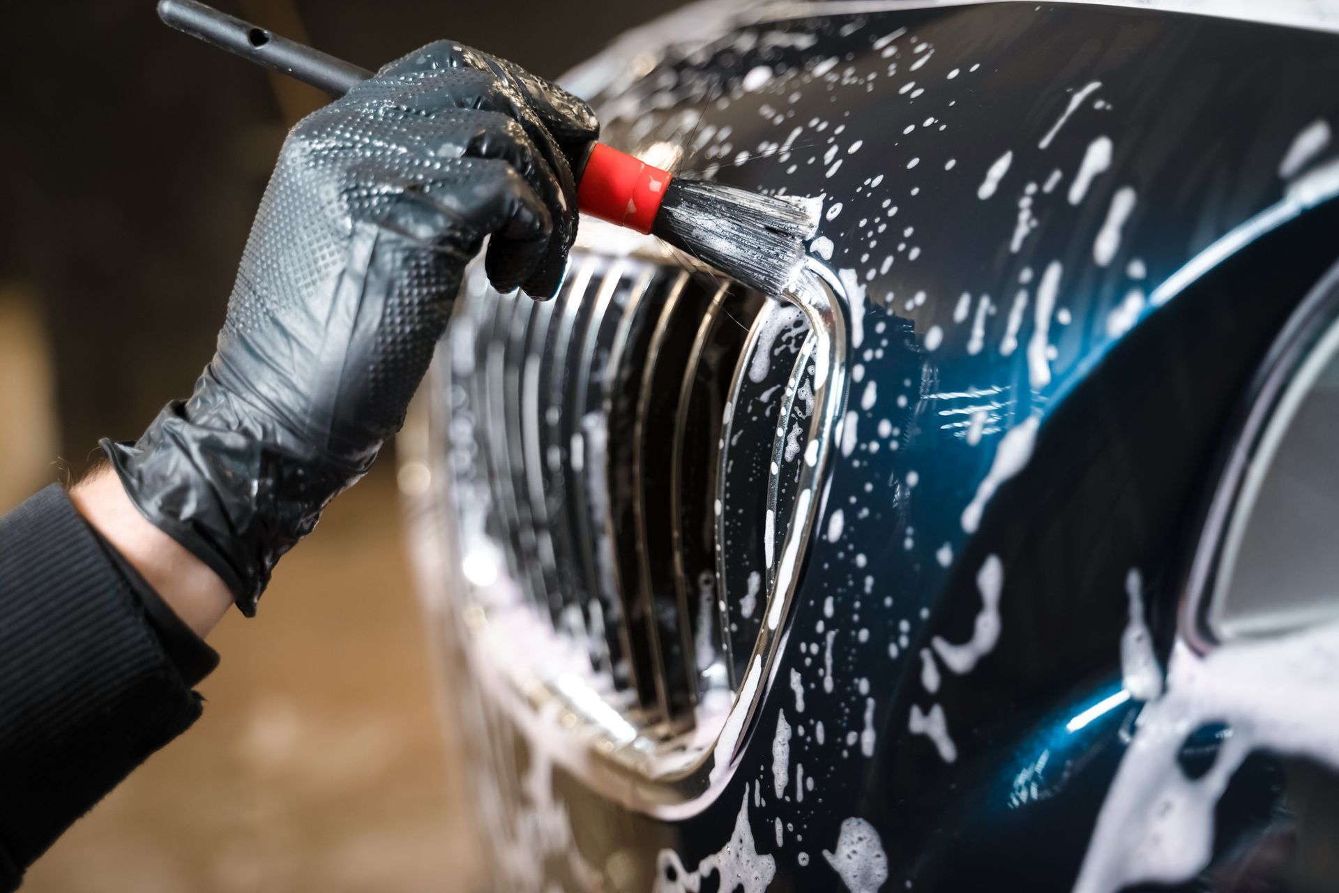 Person in black gloves applying soapy foam to a car with a spray gun.