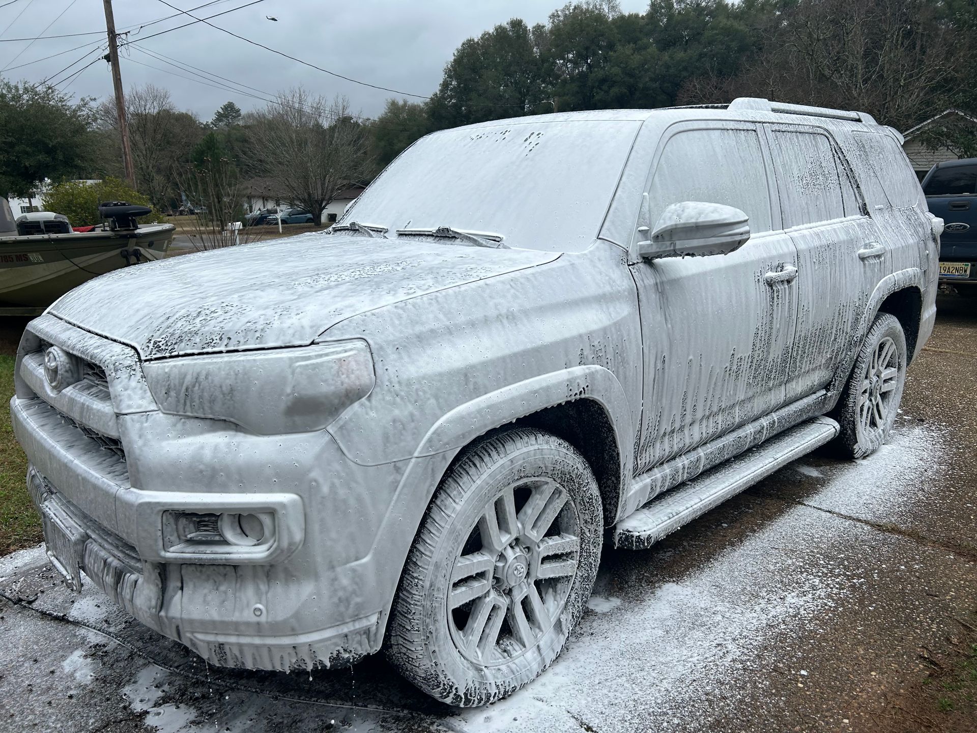 White SUV covered in foamy soap suds, outside on a driveway.
