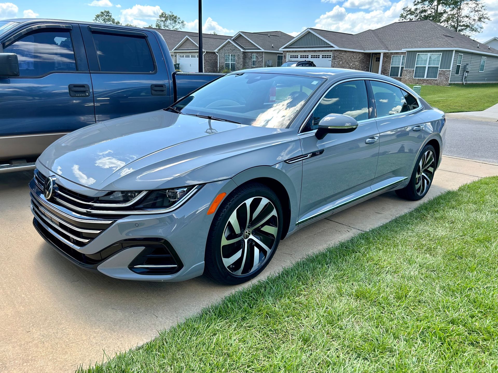 Gray Volkswagen Arteon parked on a concrete driveway in front of a house.