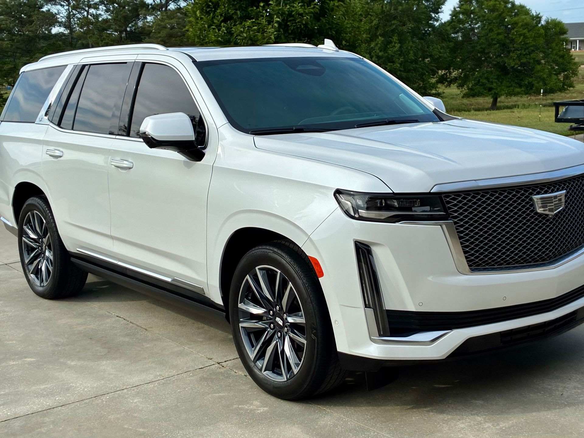 White Cadillac Escalade SUV parked on a concrete surface, with tinted windows and a chrome grill.