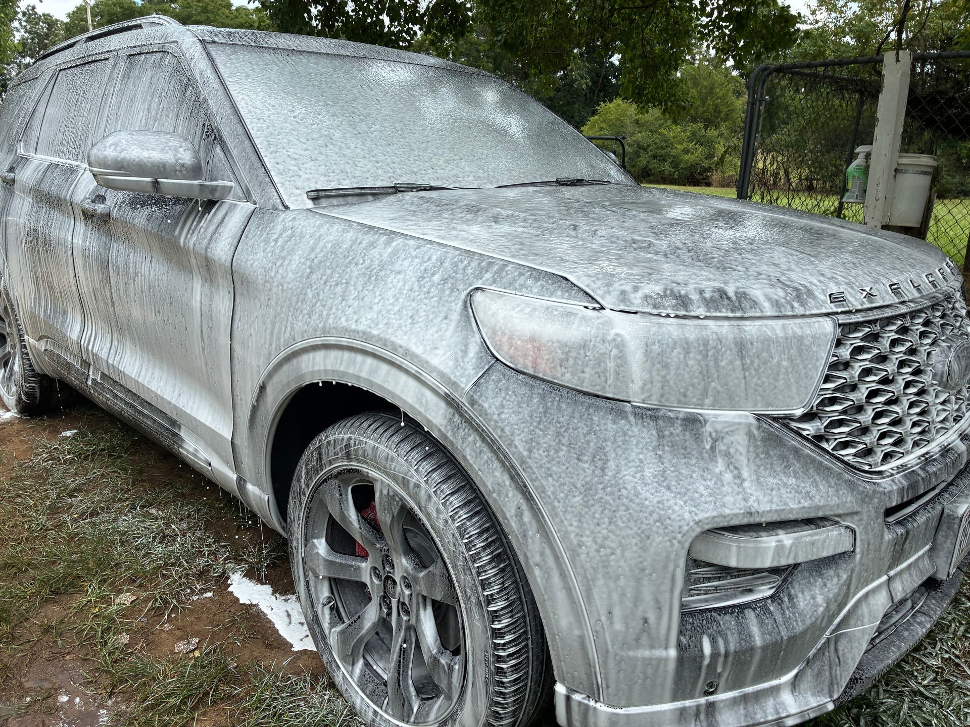 SUV covered in white soap suds, ready for washing, outdoors.