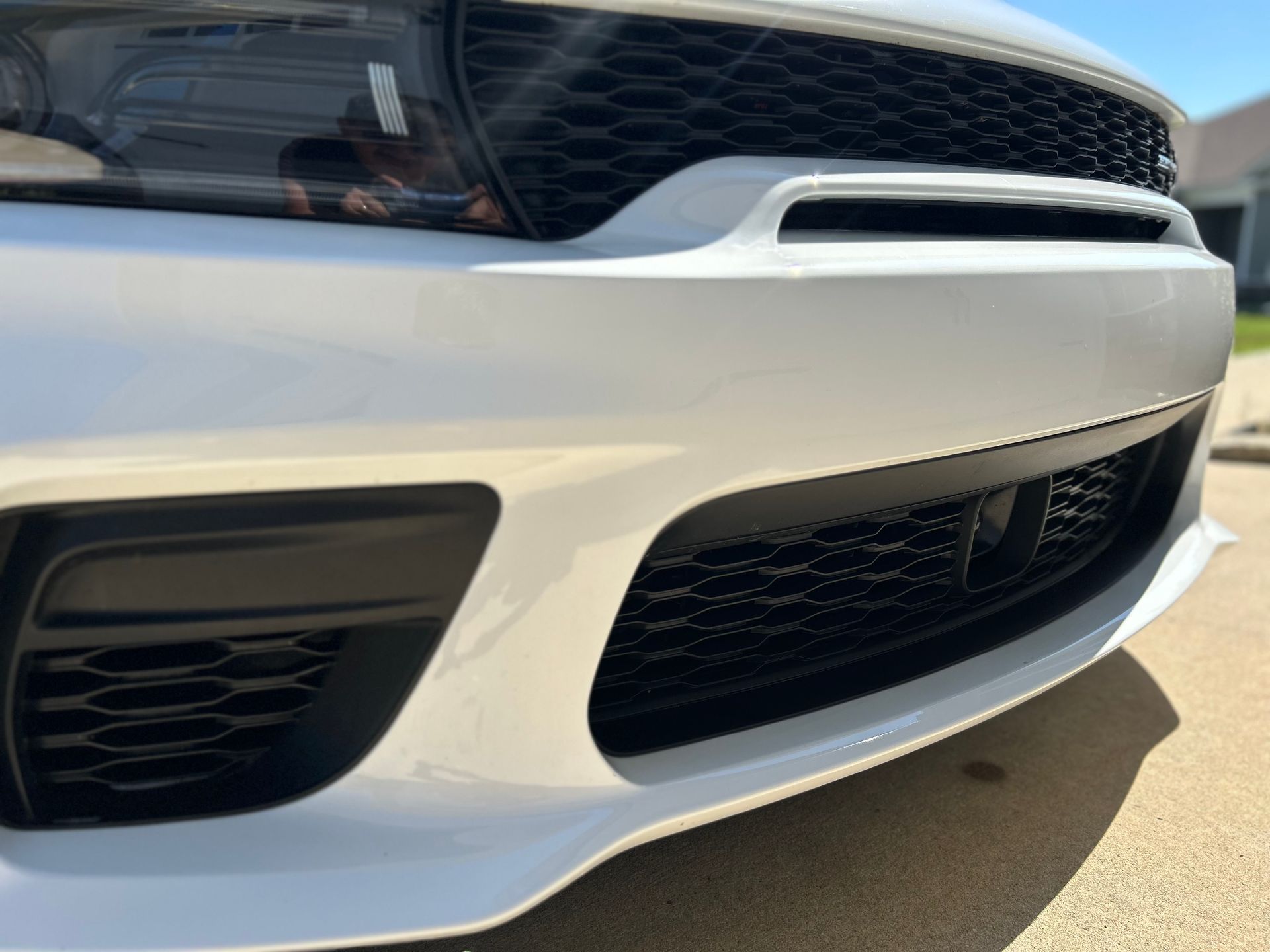 White car's front bumper with black grilles, angled close-up view outdoors, sunny day.