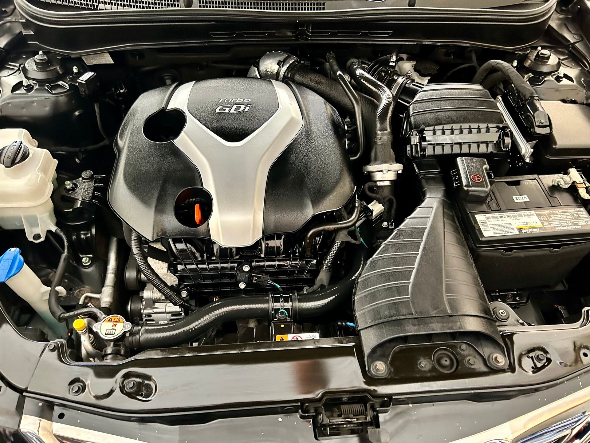 Car engine bay, black and silver, with various components and a battery.