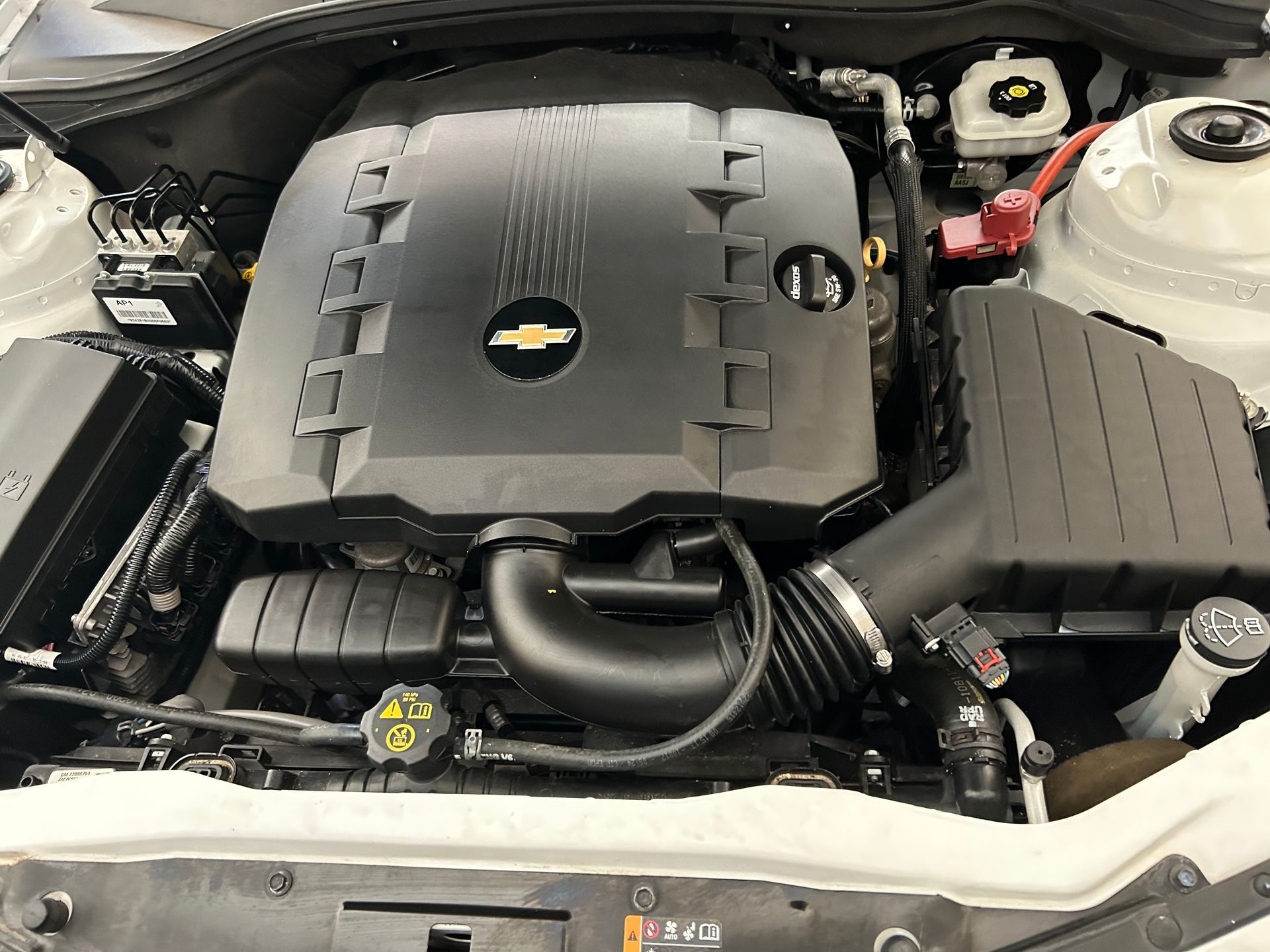 Chevrolet Camaro engine bay, black engine cover, air intake, white car.