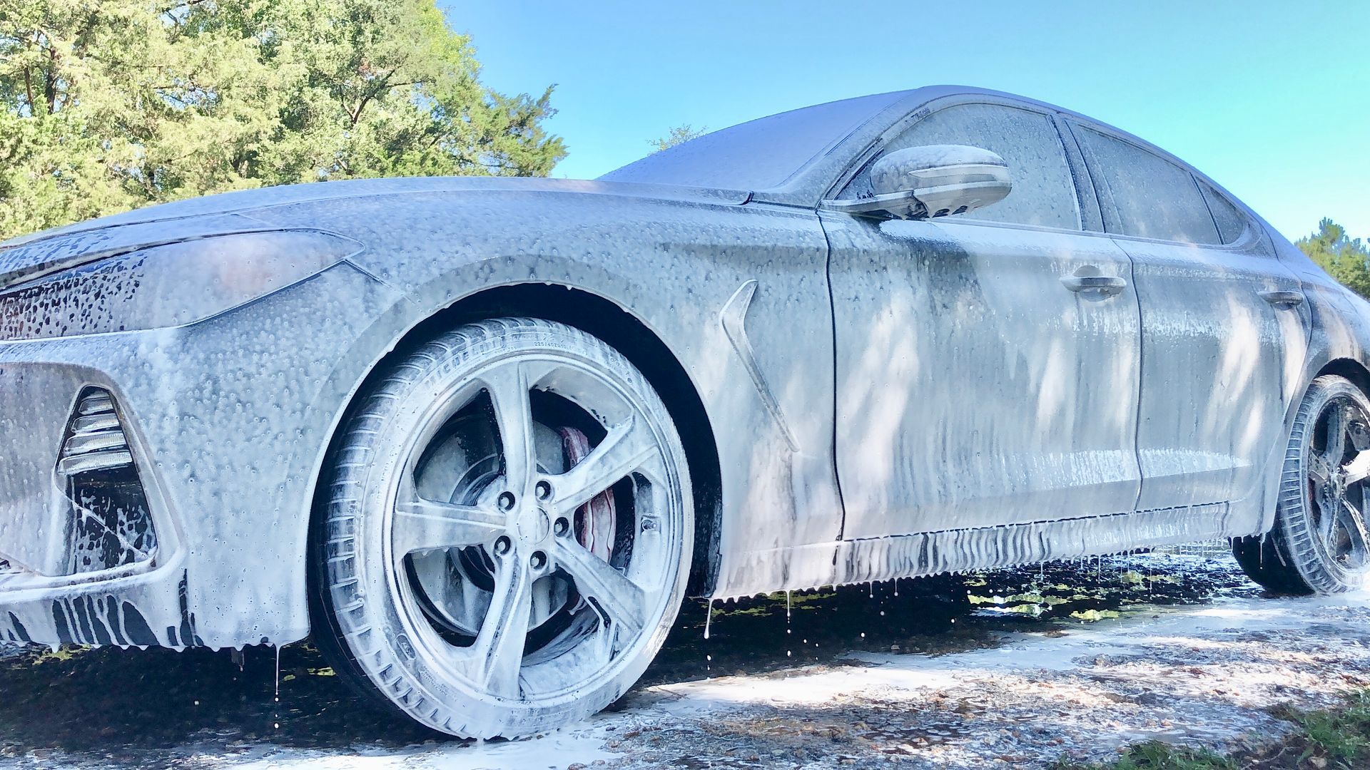 Car covered in white foam, likely being washed outdoors.