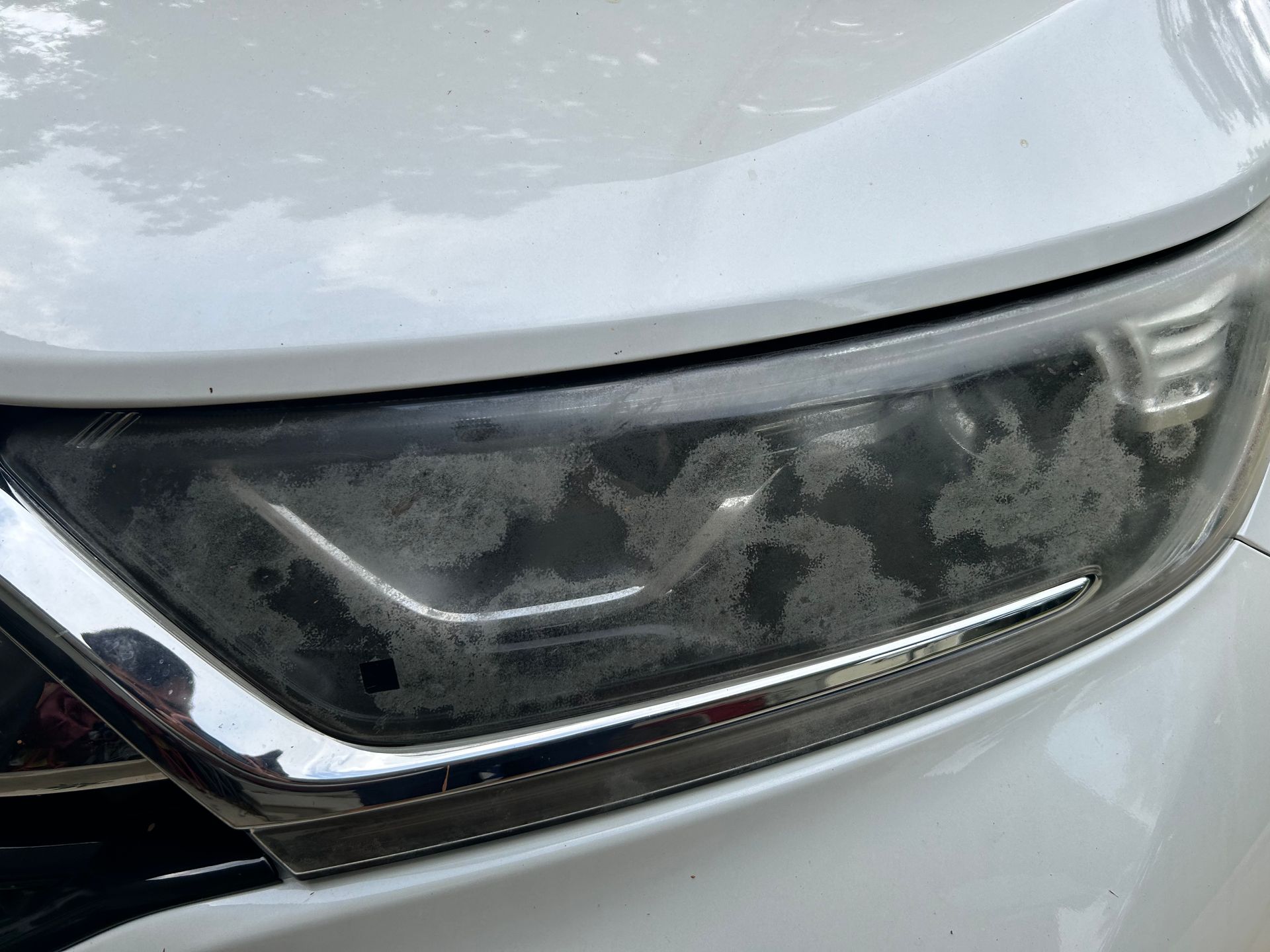 Close-up of a white car's headlight with significant clouding and degradation on the plastic lens.