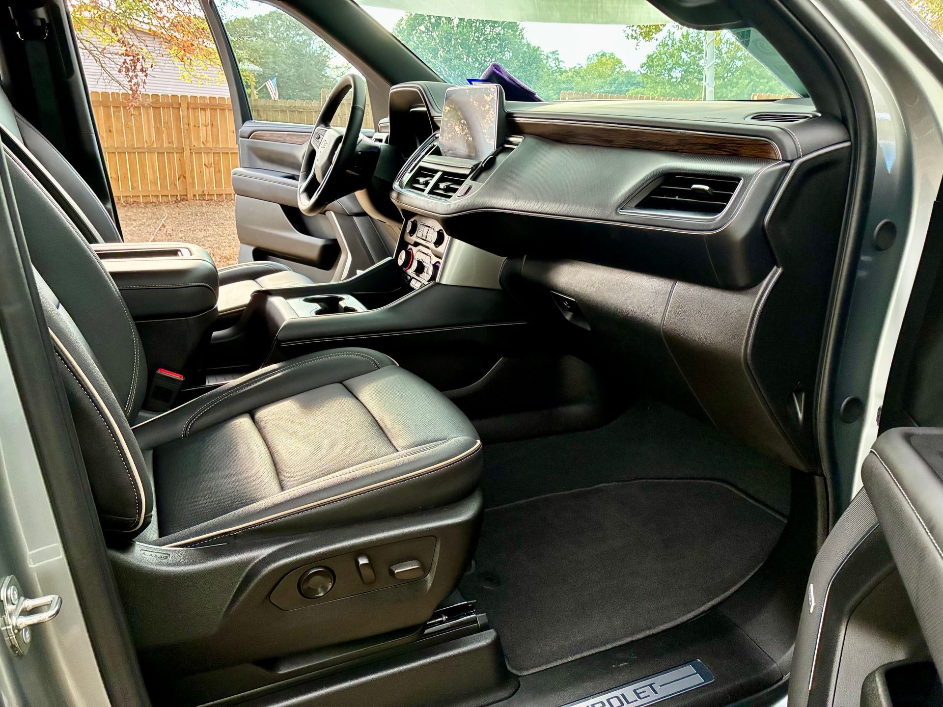 Interior view of a modern SUV, black leather seats, wood trim, and dashboard. Door open, showing exterior.