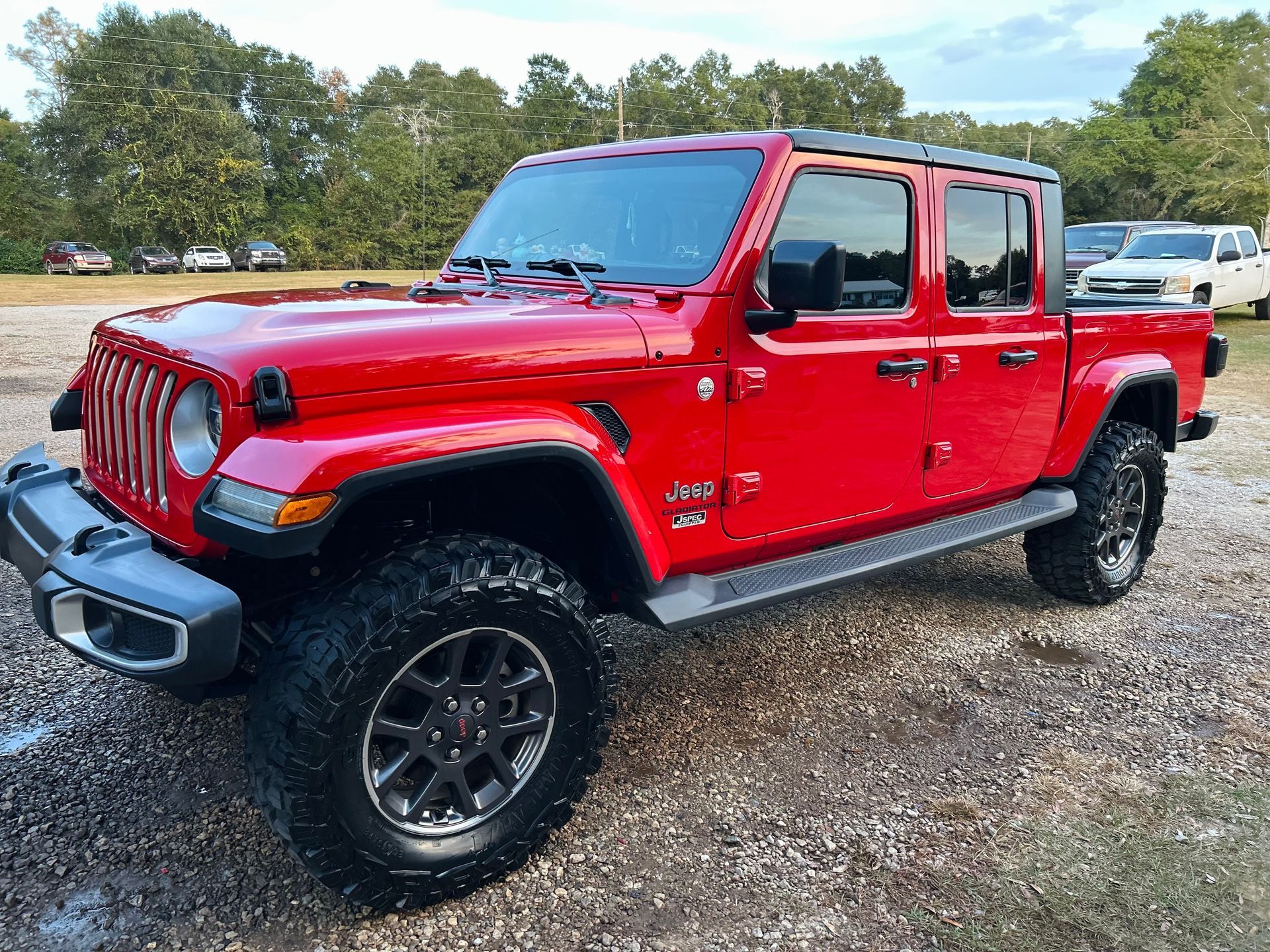 Red Jeep Gladiator truck parked on gravel, with dark tinted windows and black wheels.