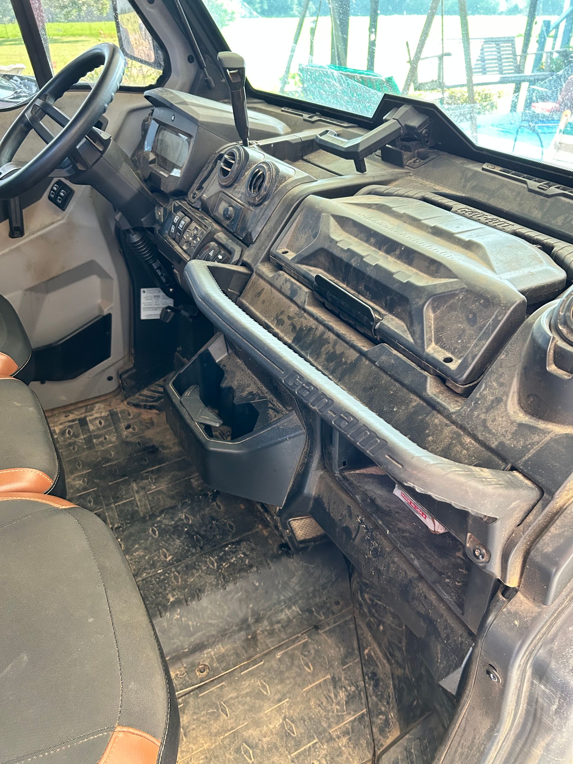 Interior of a dirty side-by-side vehicle. Black dashboard with controls, cup holder, and a black roll bar.