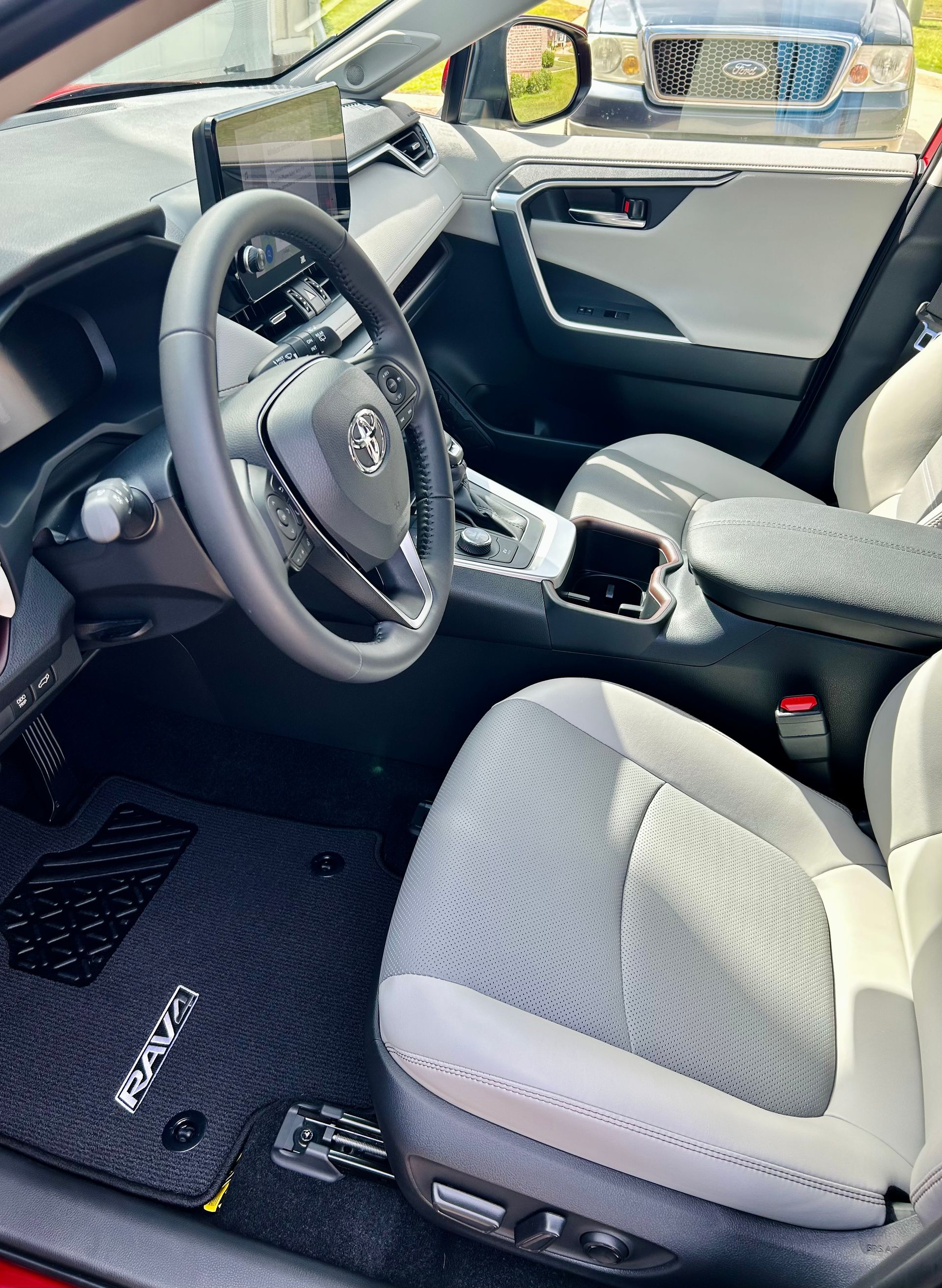 Interior of a Toyota RAV4. Gray and white seats, black steering wheel, dashboard. Black floor mats.