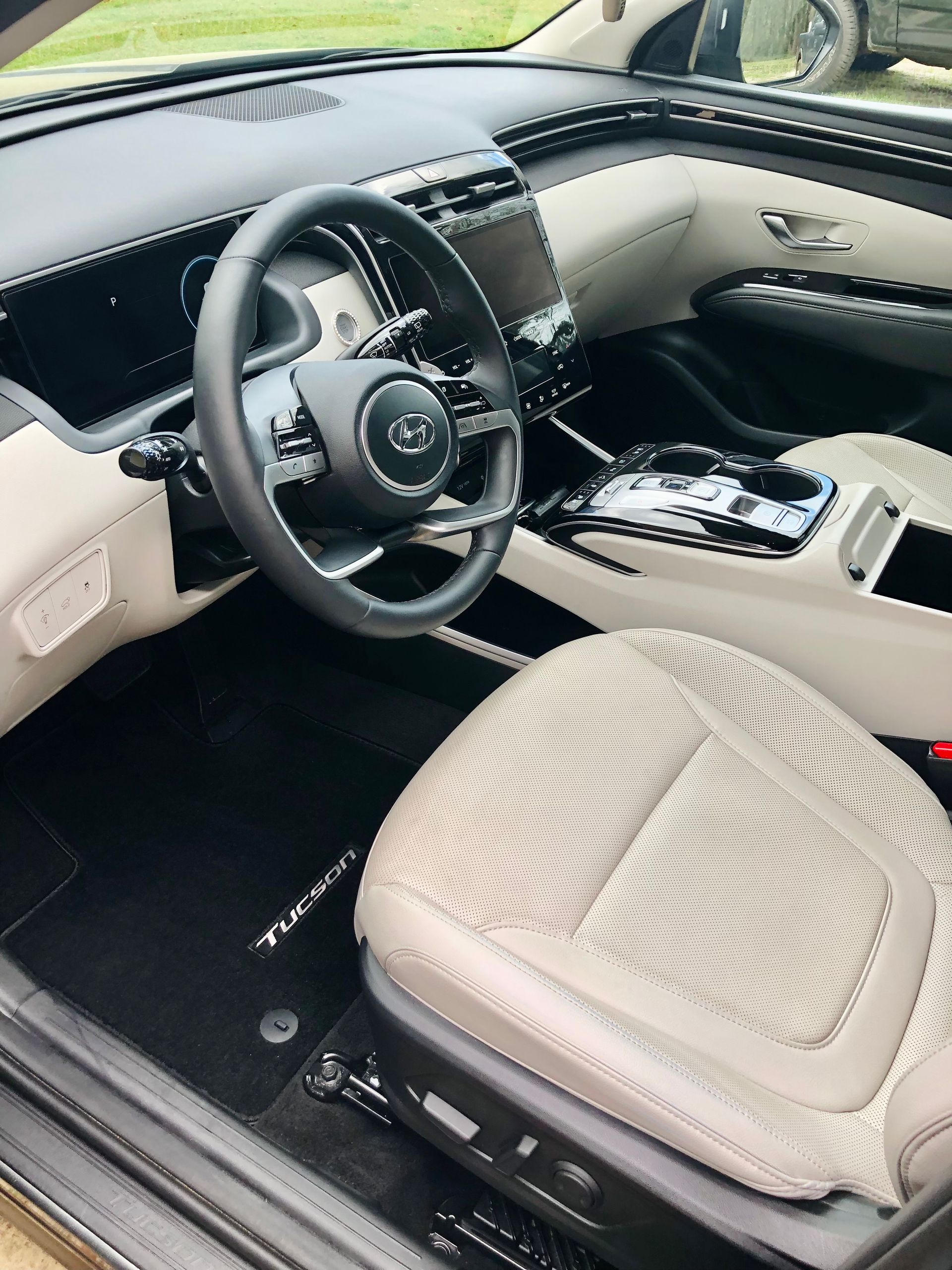 Interior view of a beige and black car. Steering wheel, dashboard, and seat visible.