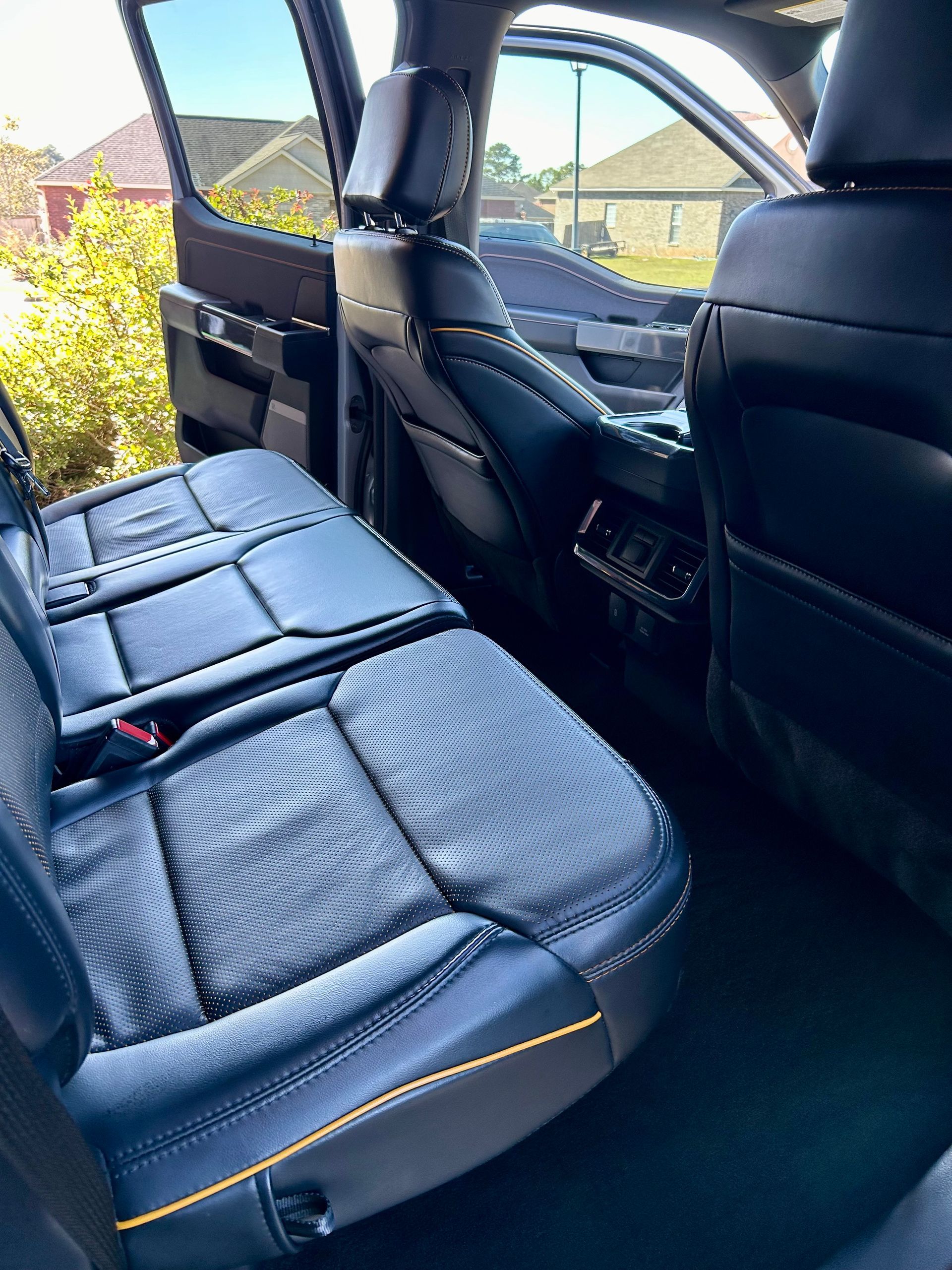 Black leather truck backseat with yellow stitching, open door, and exterior view.