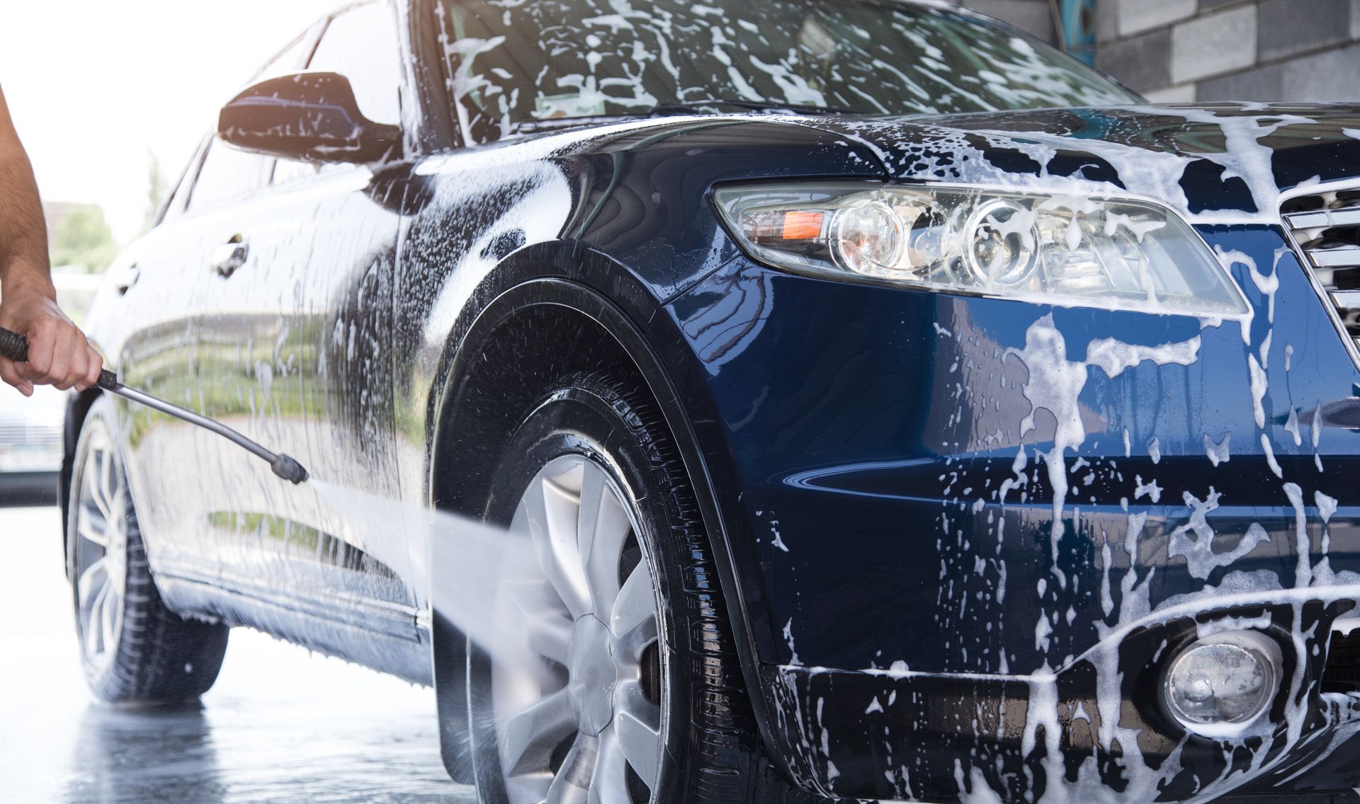 A dark blue car being washed with soapy water at a car wash.