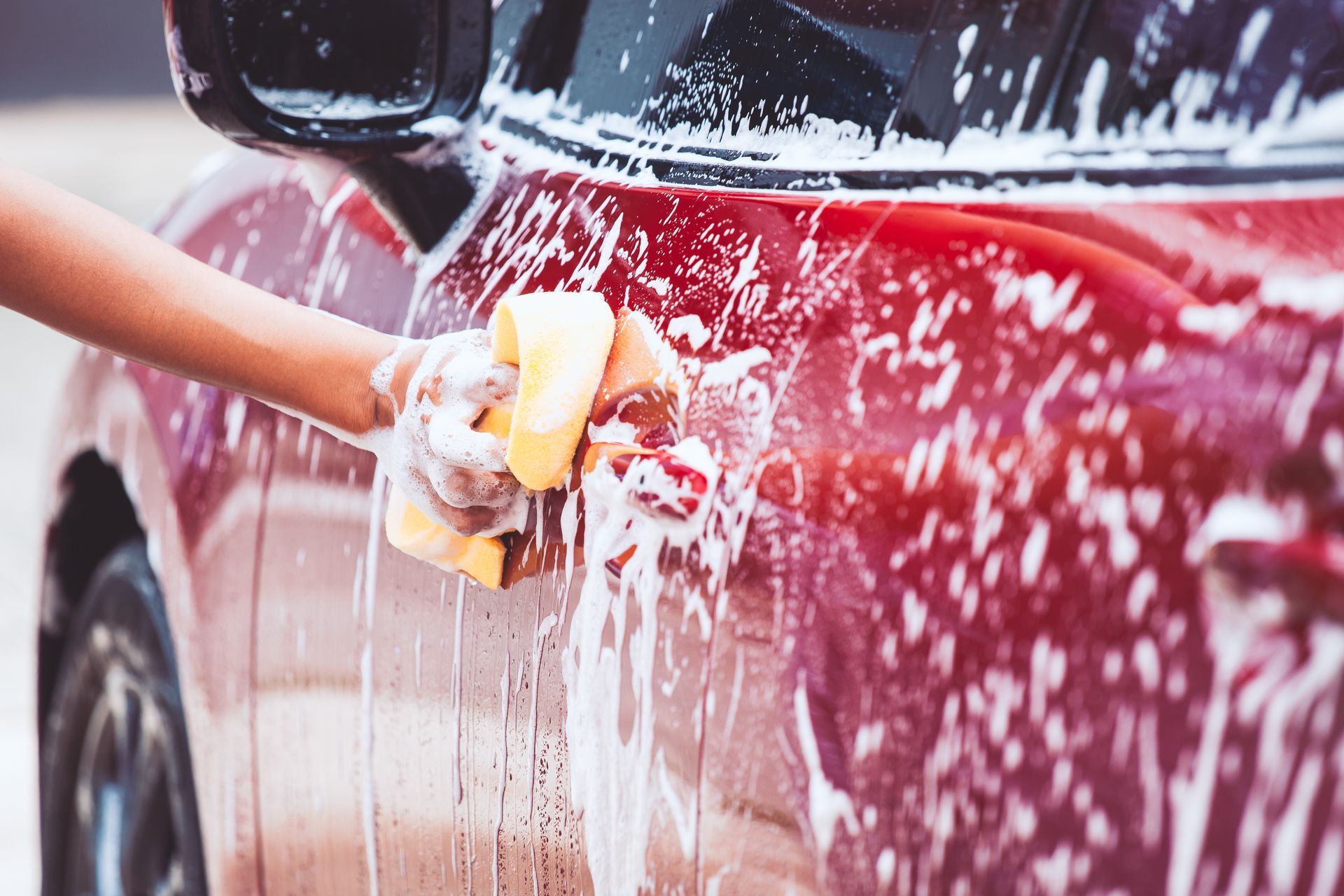 Person washing a red car with a soapy sponge.