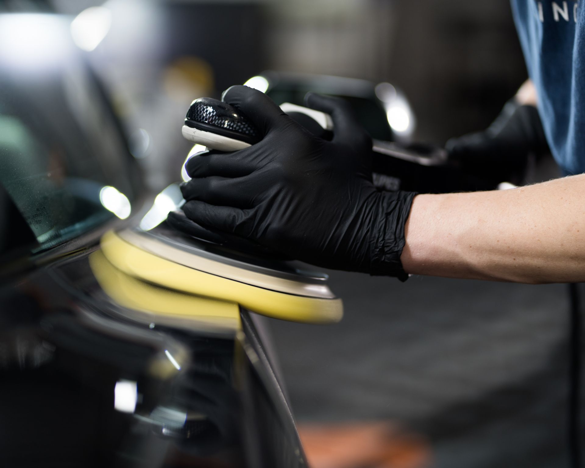 Person wearing black gloves polishing car with yellow and black buffer.