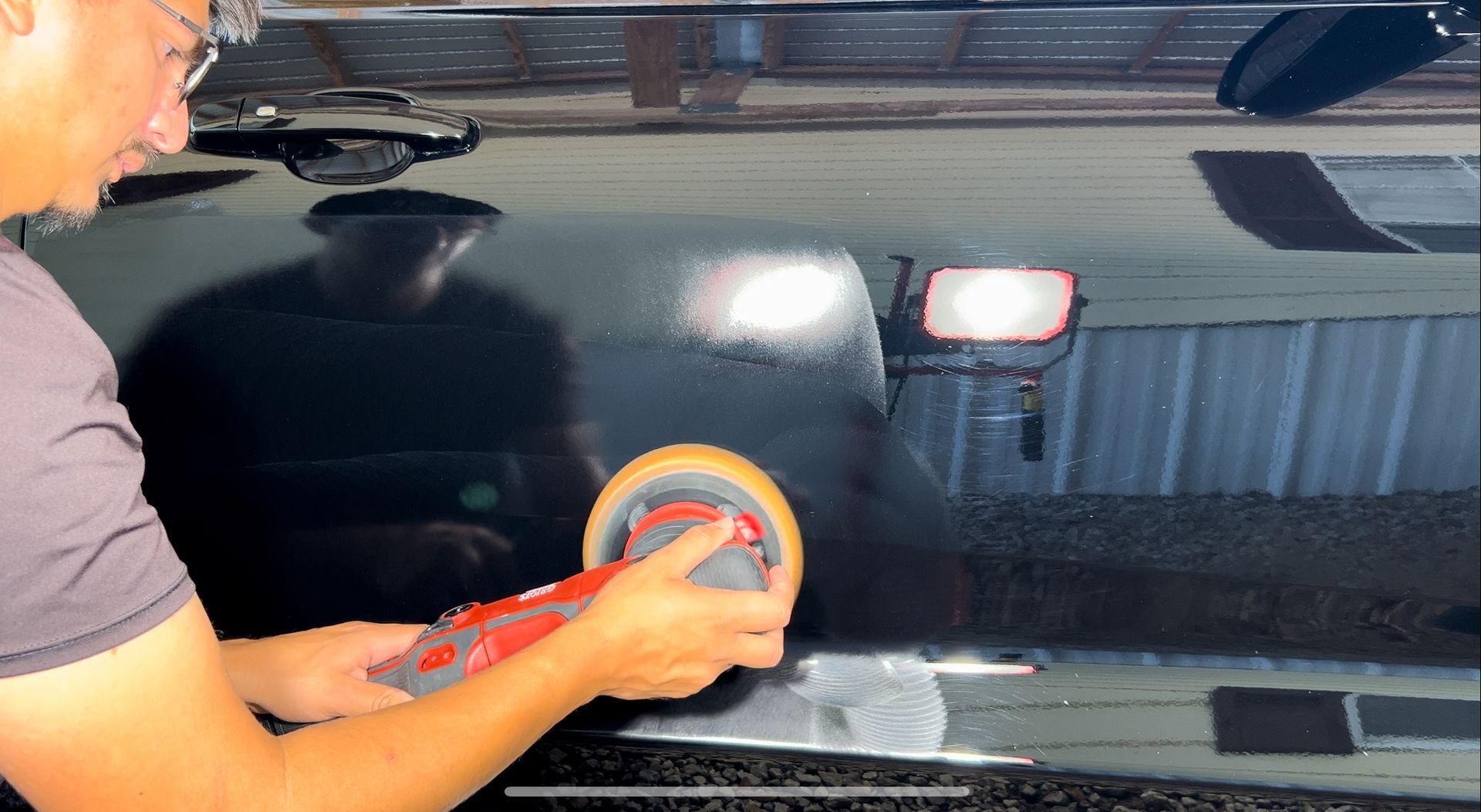 Person using an electric polisher on a black car, in a well-lit garage.
