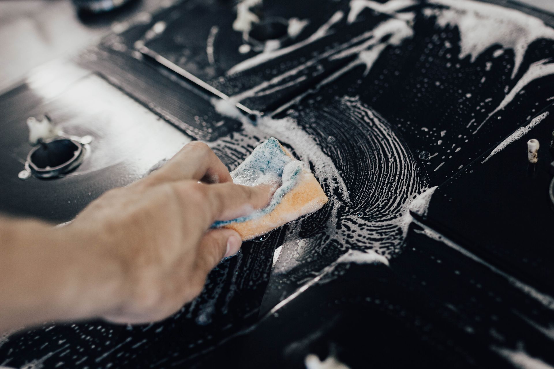 Person polishing a red car's hood with a rotary buffer, wearing black gloves.