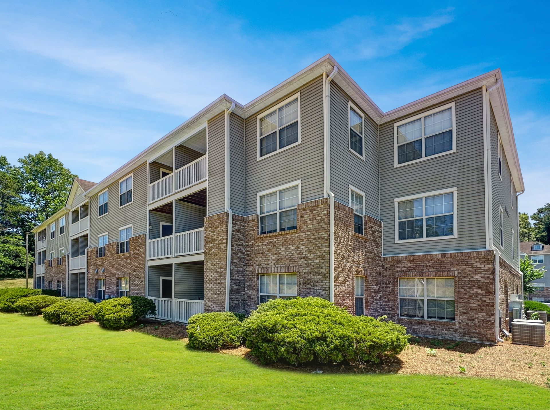 A large apartment building with a lot of windows and a lush green lawn in front of it.
