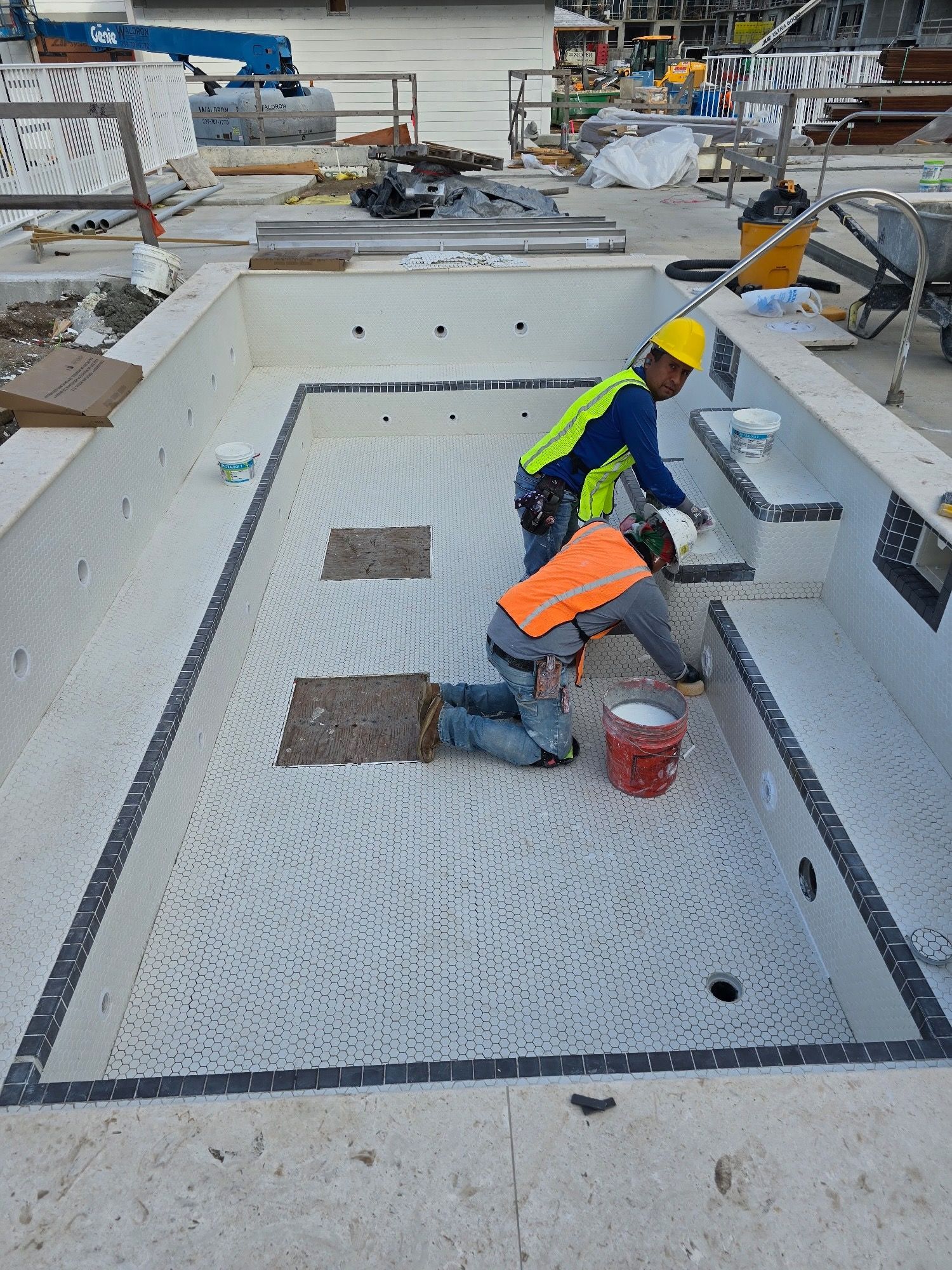 Two construction workers are working on a swimming pool.