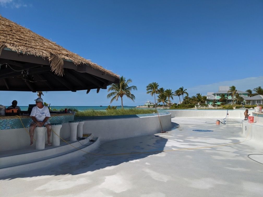A man sits at a bar overlooking a swimming pool