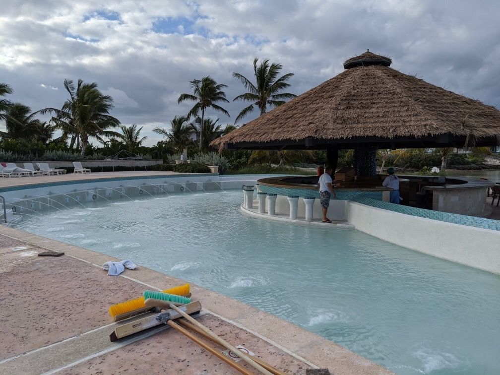 A man is standing on the edge of a swimming pool under a thatched roof.