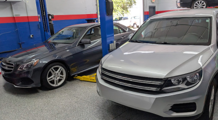 Cars in a repair shop: a silver SUV and a dark sedan on a lift - Bimmerfix