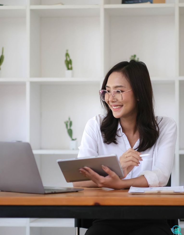 A smiling marketing professional reviews a digital growth plan on a tablet while working on a laptop in a modern office, representing strategic planning and campaign setup at Growth Reach Digital