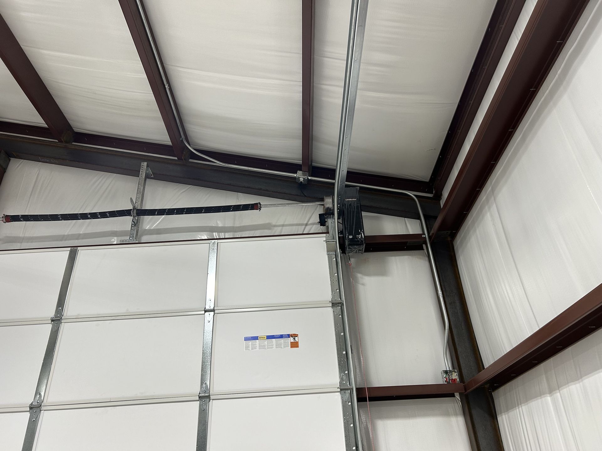 Garage door and opener inside a metal building with insulation.